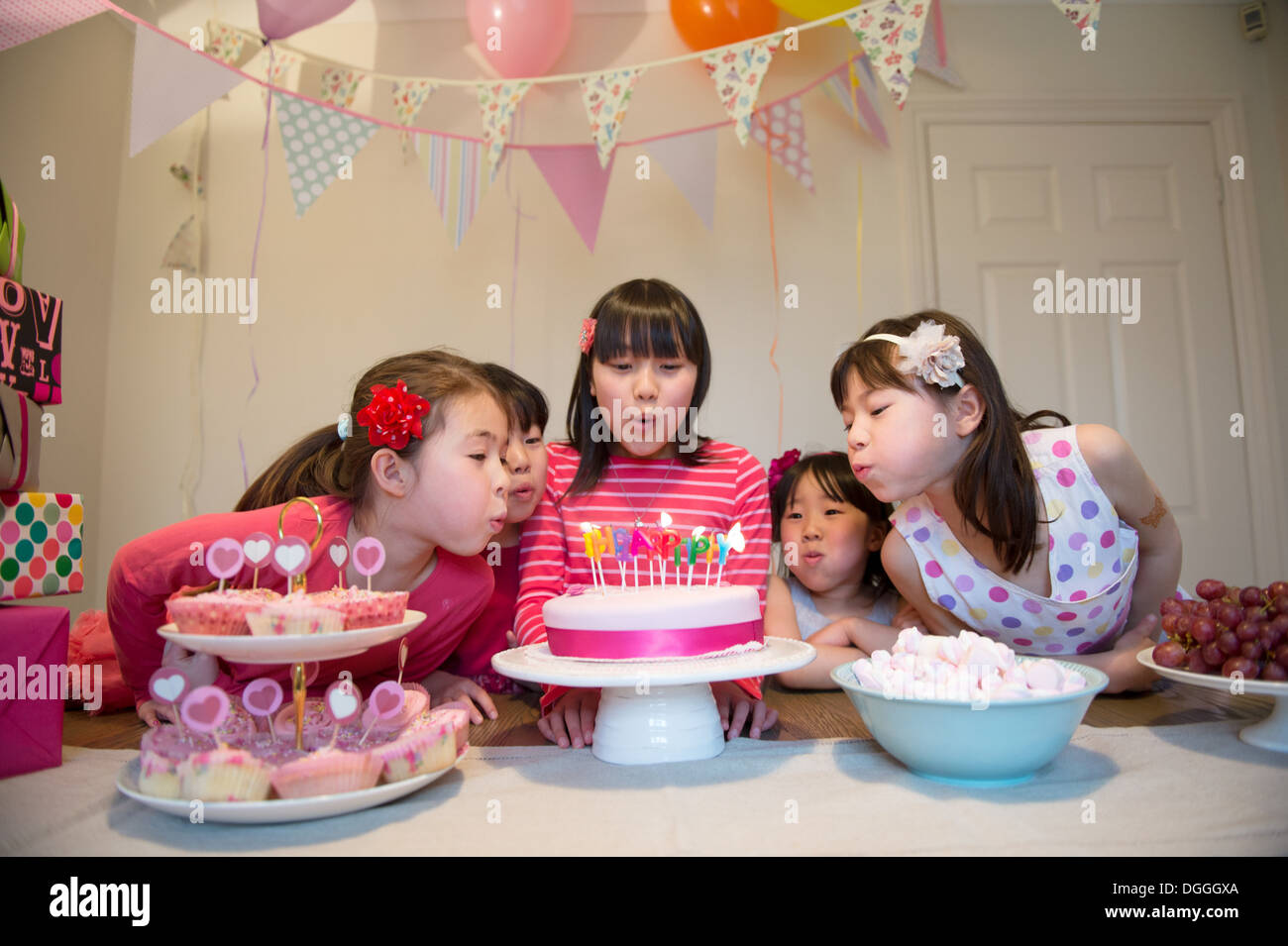Mädchen bläst Geburtstagskerzen auf Kuchen Stockfoto