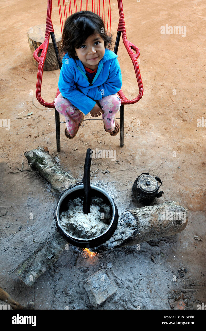 Mädchen, 5, sitzen am Kamin mit einem Topf Porridge, in einer Gemeinschaft der Guarani-Indianer, Jaguary, Caaguazu Abteilung Stockfoto