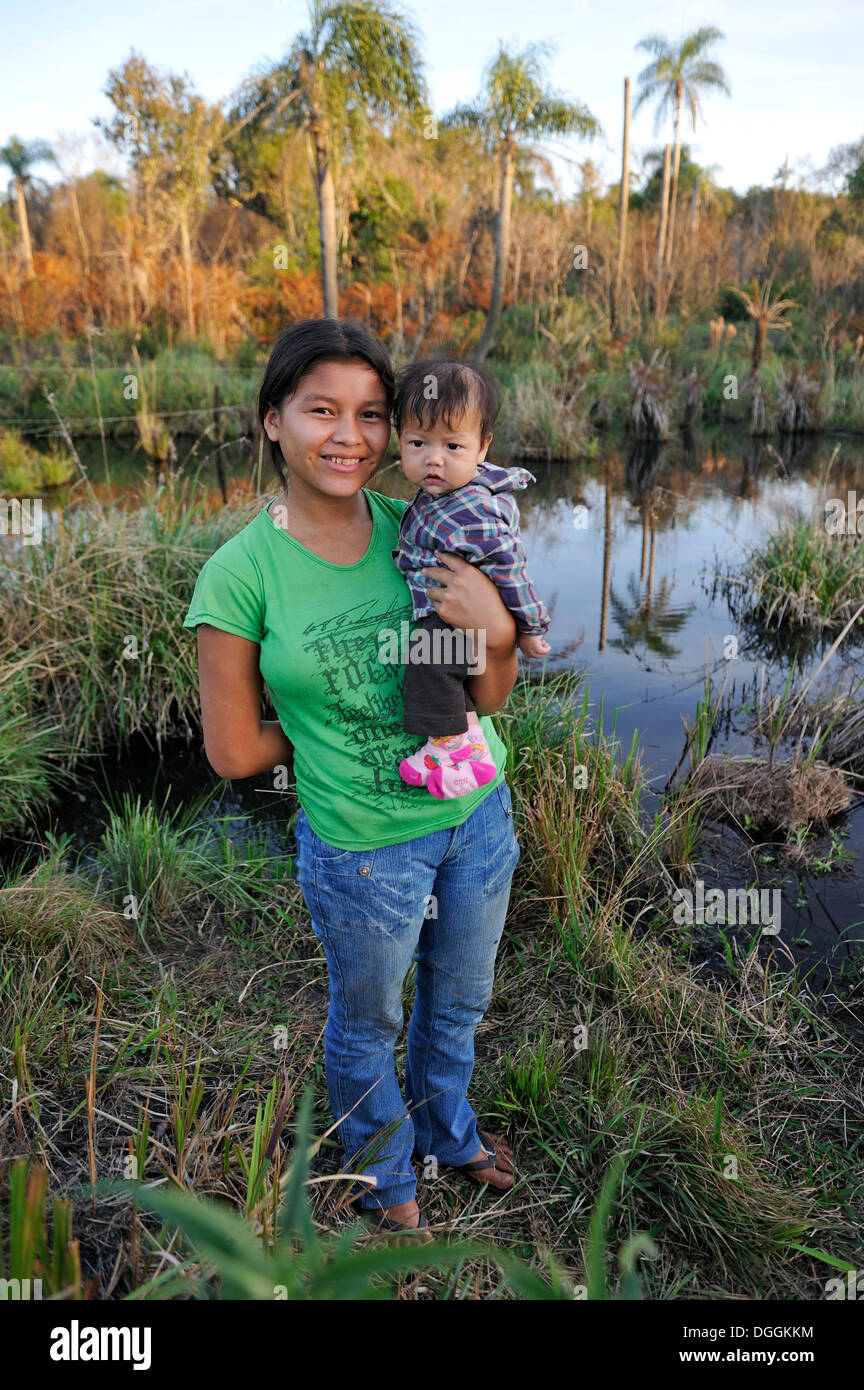 Junge Mutter mit einem Kind im Arm vor einem Teich in der Gemeinschaft der Mbya-Guarani-Indianer, Campito Stockfoto