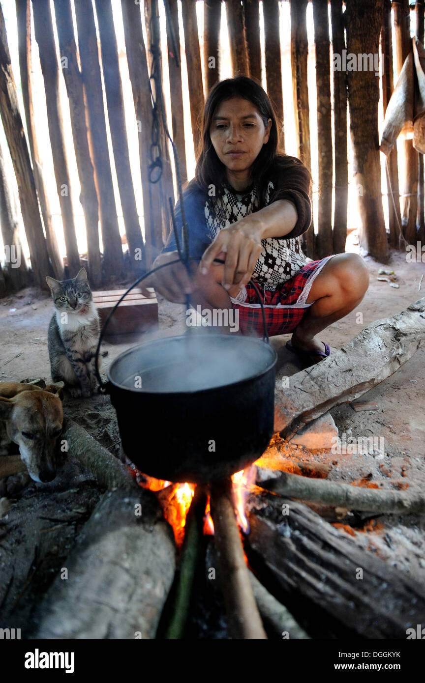 Frau, 34, Kochen Cassava oder Maniok (Manihot Esculenta) in einem Topf über dem offenen Feuer in einer einfachen Küche, in der Gemeinde Stockfoto