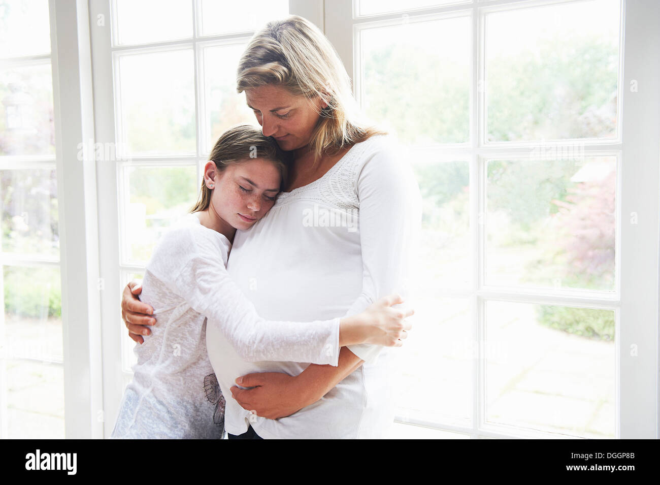 Schwangere Mutter mit Tochter im Teenageralter durch Fenster Stockfoto