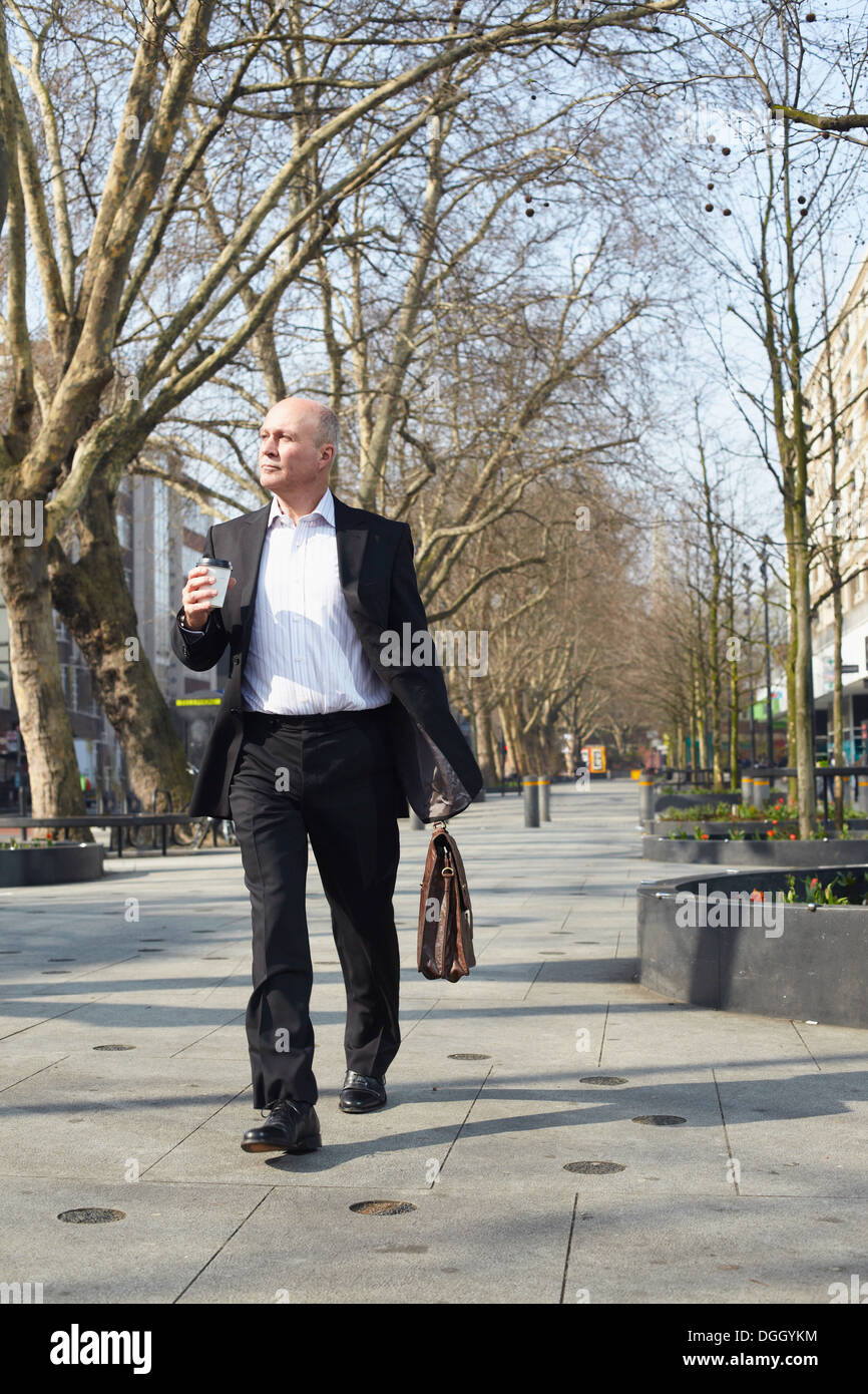 Reife Geschäftsmann zu Fuß auf dem Bürgersteig mit Kaffee Stockfoto