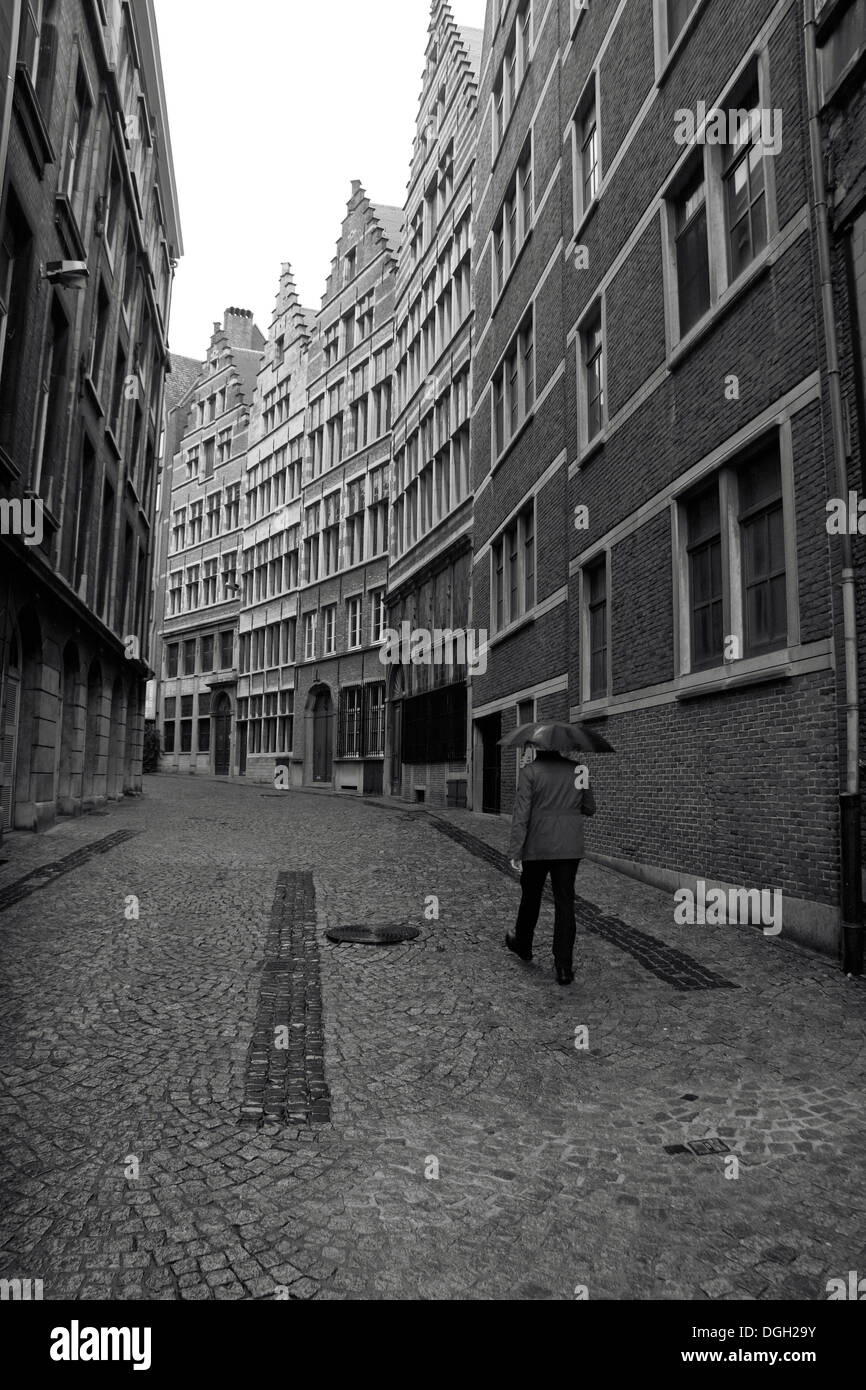 Ein Mann hält einen Regenschirm geht auf einer gepflasterten Straße (Kaasstraat) mit überragenden Eigenschaften in Antwerpen, Belgien. Stockfoto