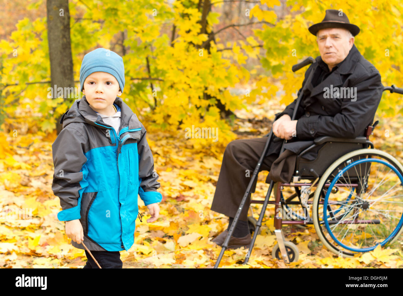 Kleiner Junge mit seinem behinderten Großvater sitzt in einem Rollstuhl hält seine Krücken genießen einen Tag in der Natur spielen zusammen in bunten gelb Herbst Bäume in einem Park. Stockfoto