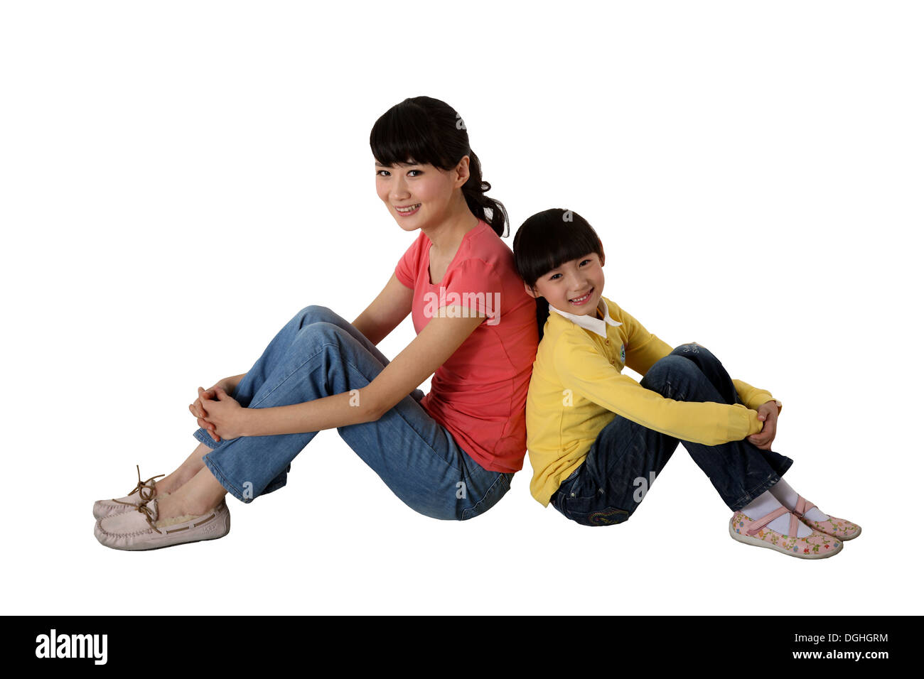Ostasiatische Mutter und Tochter sitzen auf dem Boden Rücken an Rücken, Knie, greifen, lächelt und schaut in die Kamera Stockfoto