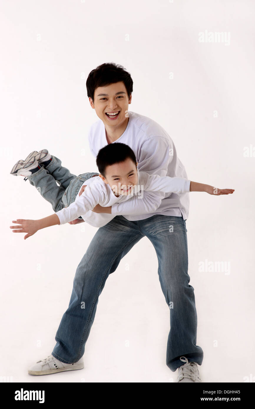 Ostasiatische Vater halten Sohn oben in der Luft fliegen, Sohn lächelnd, Blick in die Kamera Stockfoto