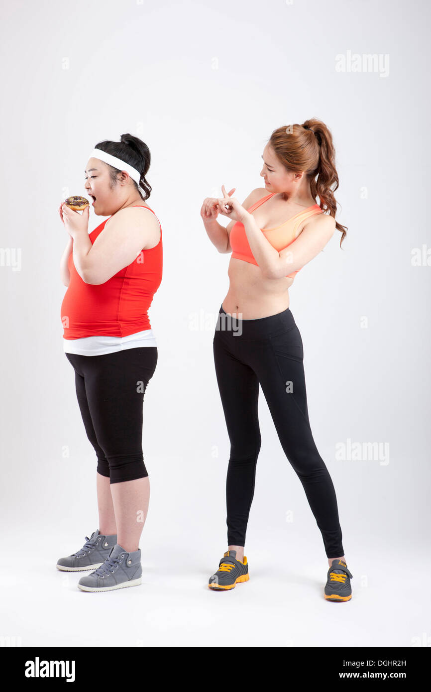 ein dickes Mädchen mit einem Donut und ein dünnes Mädchen in Sportkleidung Stockfoto
