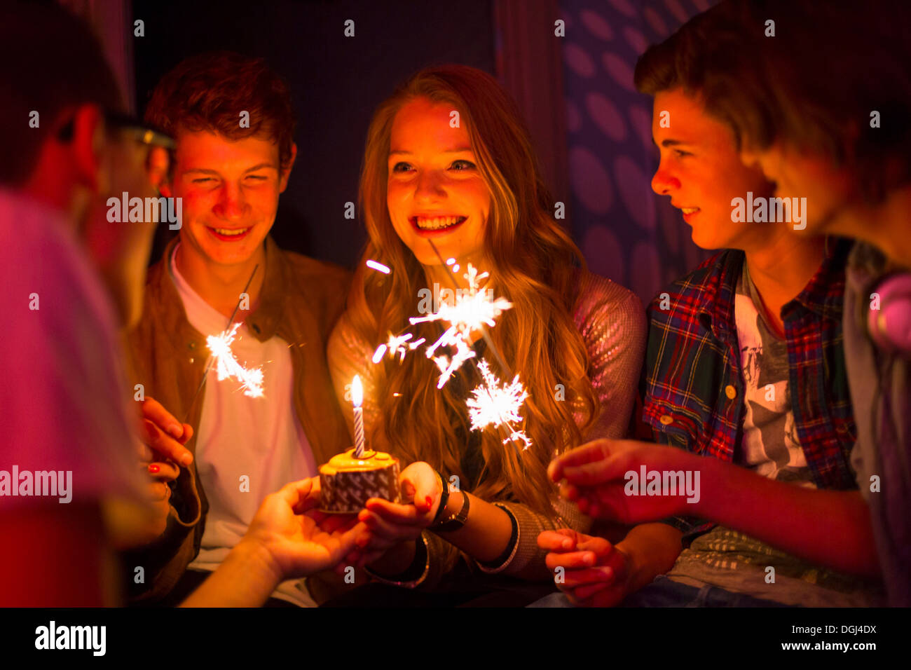Gruppe von Jugendlichen, die herumsitzen und Geburtstagstorte mit Wunderkerzen Stockfoto