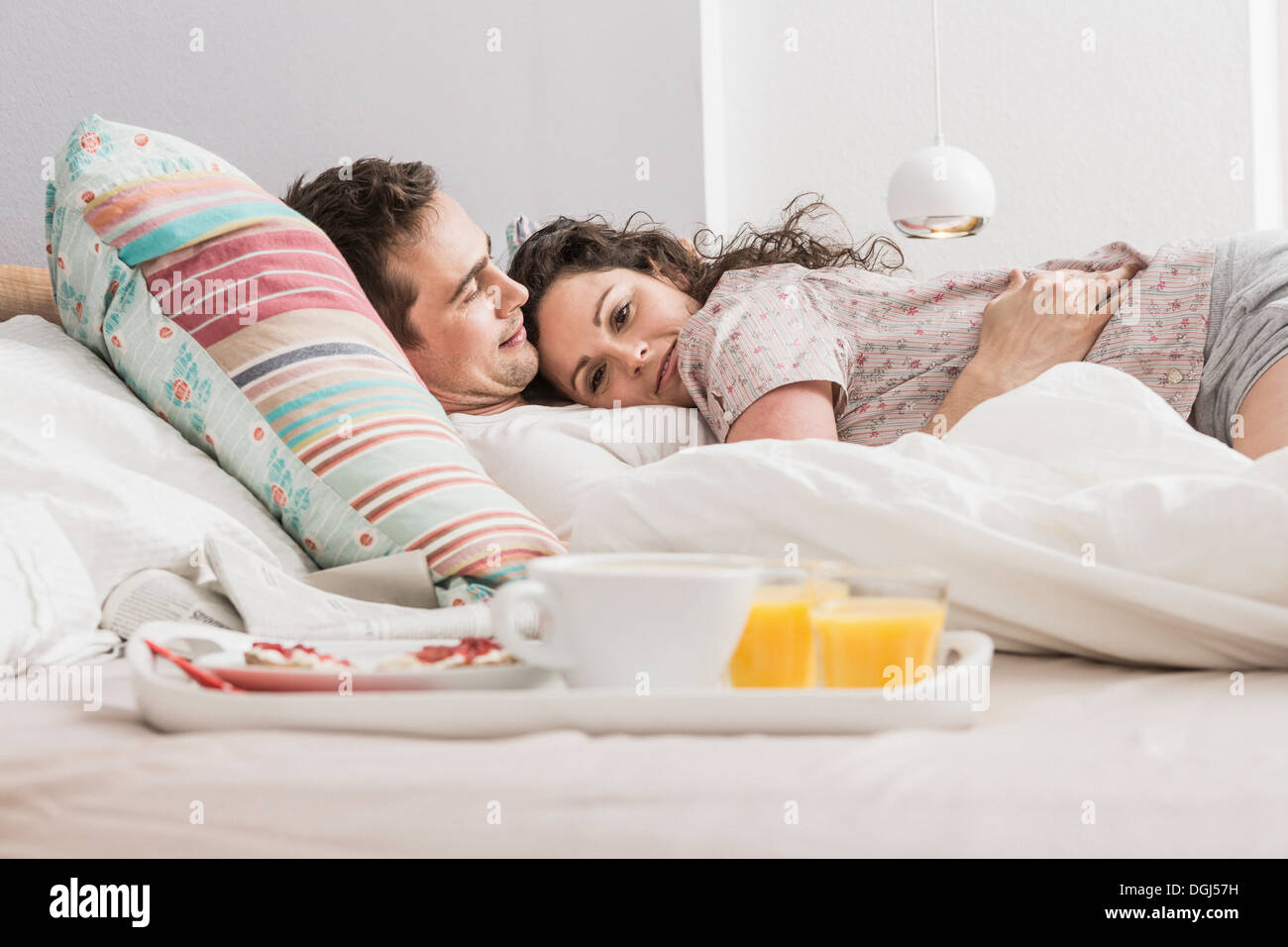 Mitte erwachsenes paar im Bett liegend, Frühstück auf Tablett, umarmen Stockfoto