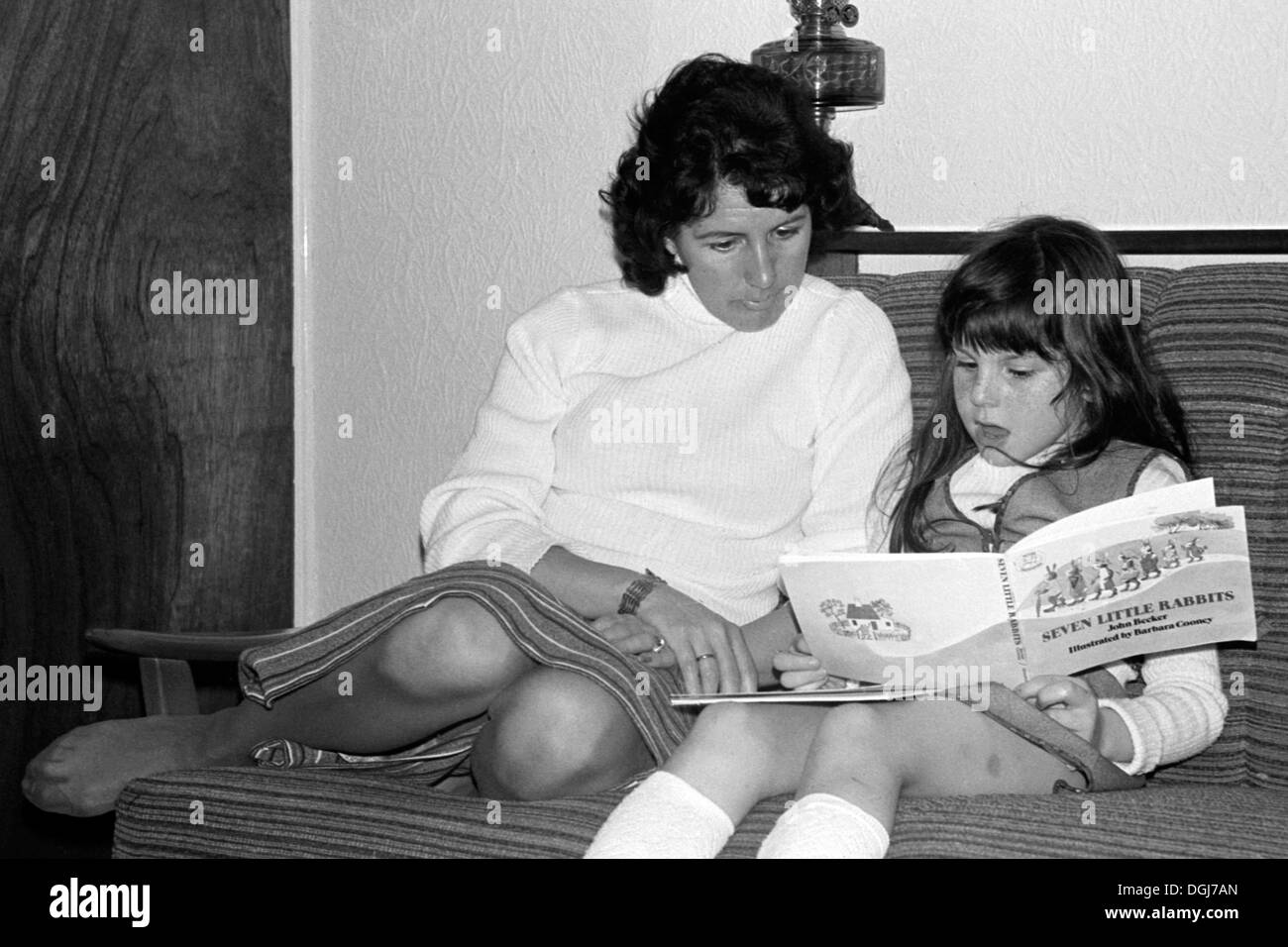 Mutter wacht über junge Tochter, wie sie ihre Lesung während der 1970er Jahre Großbritannien praktiziert Stockfoto