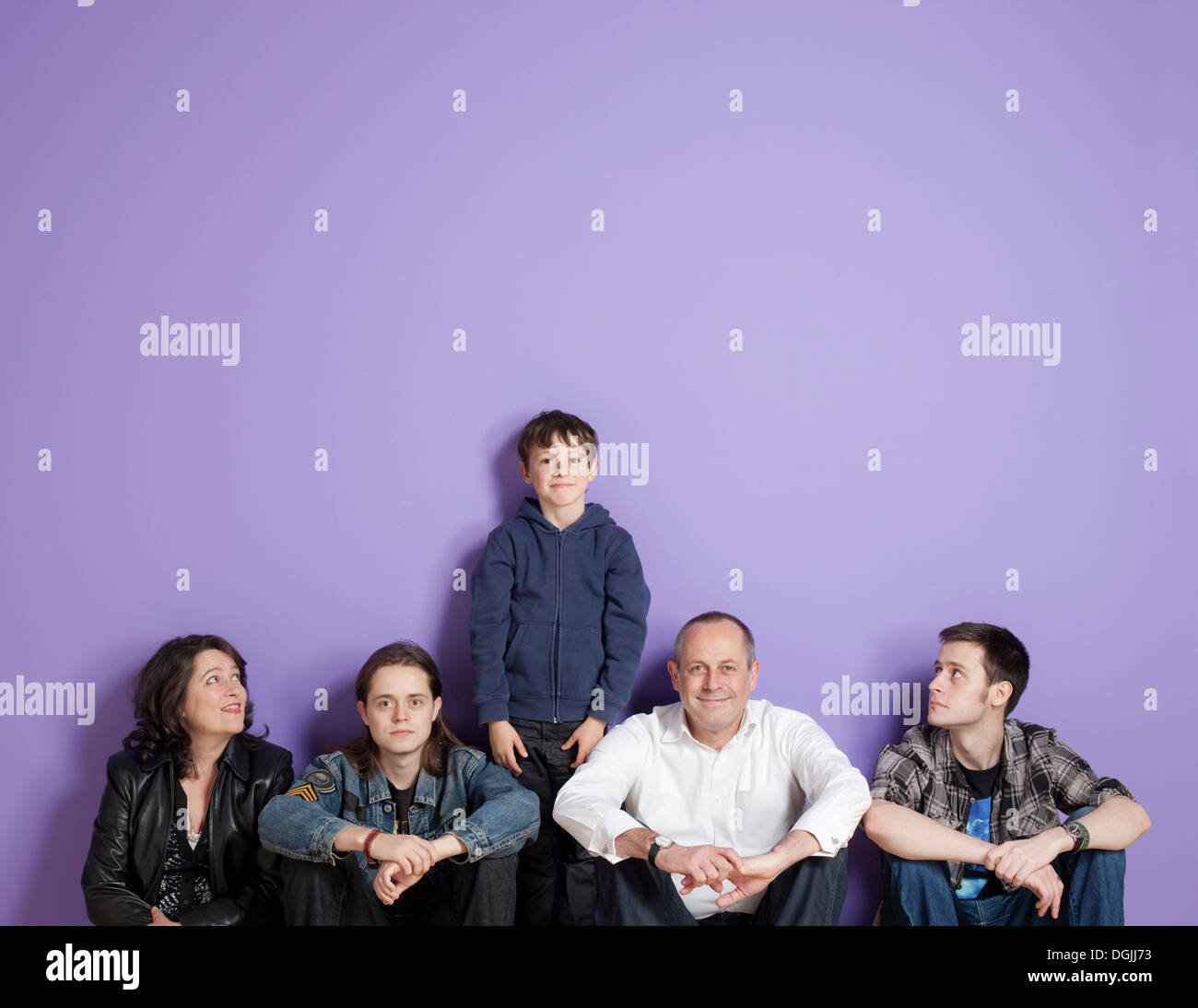 Junge steht in der Mitte sitzt Familie vor lila Hintergrund Stockfoto