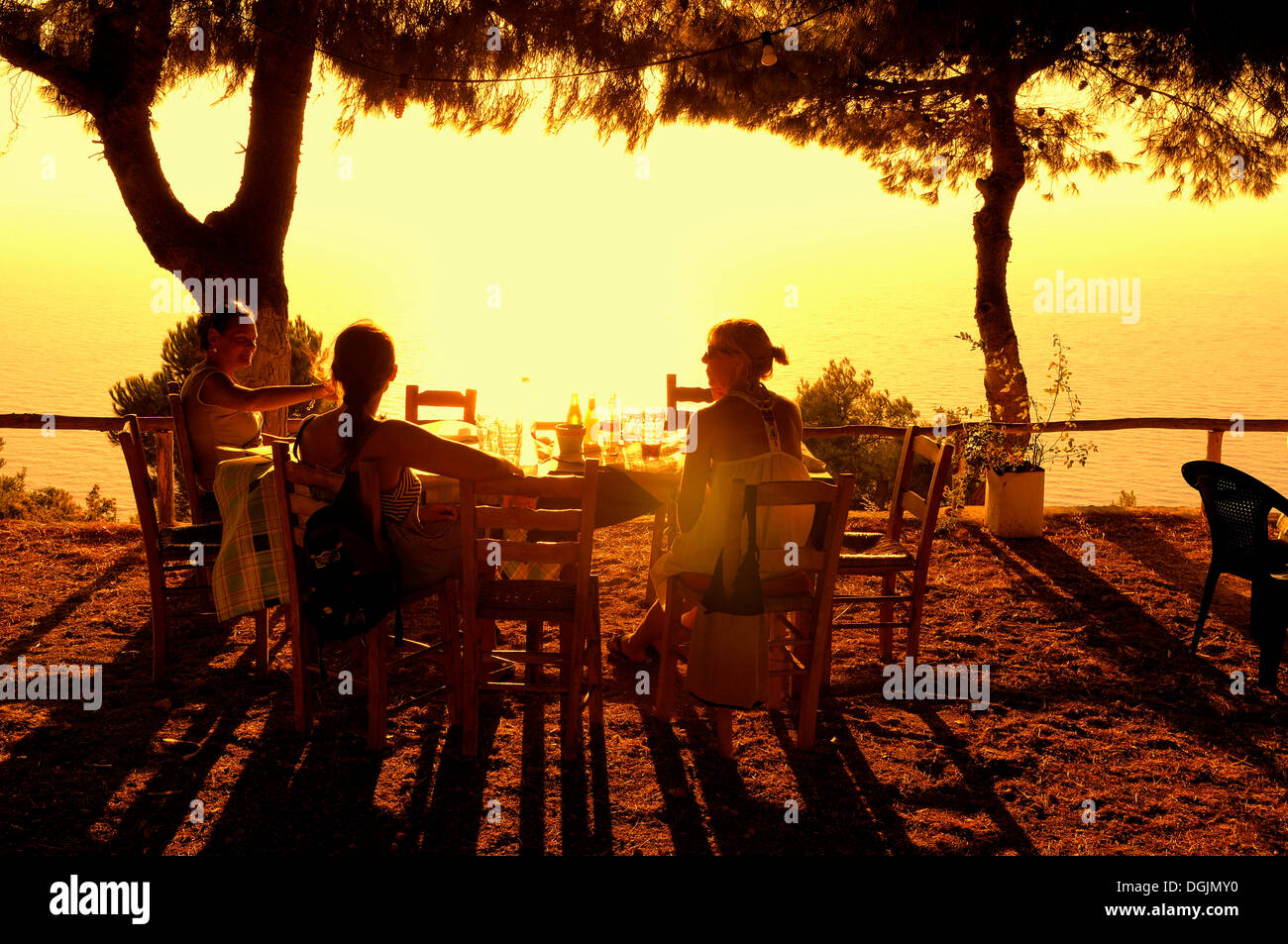 Drei Frauen sitzen an einem Tisch bei Sonnenuntergang, Abendstimmung im griechischen Meer Garten, Lefkas oder Lefkada, Griechenland, Europa Stockfoto