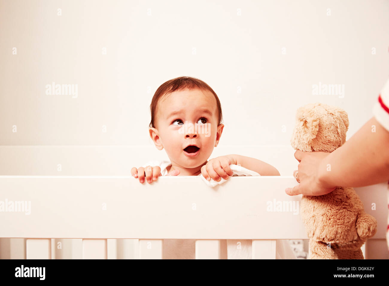 Baby auf der Suche über Krippe, Blick auf Mutter mit Stofftier Stockfoto