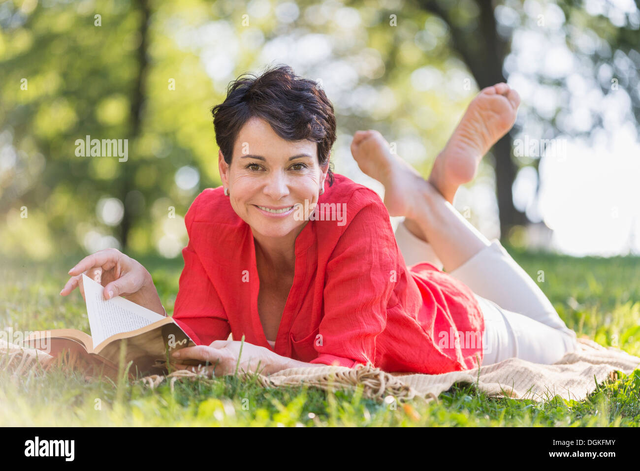 Reife Frau liegend auf dem Rasen und Buch Stockfoto