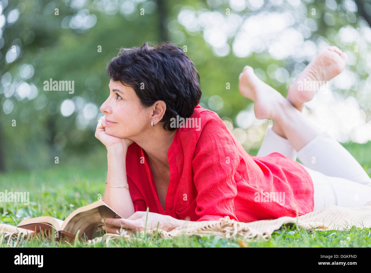 Reife Frau liegend auf dem Rasen und Buch Stockfoto