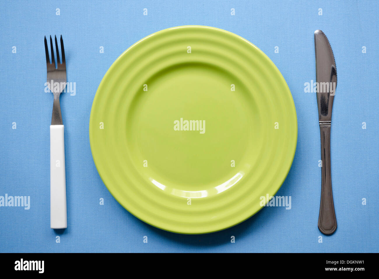grüne leeren Teller auf der blauen Tischdecke mit Messer und Gabel Stockfoto