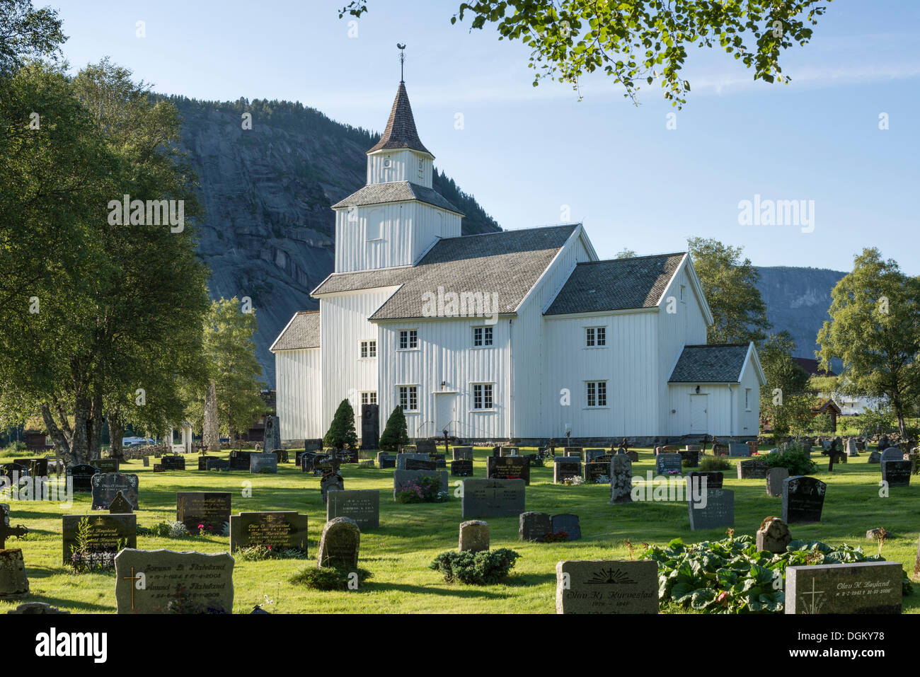 Große weiße Holzkirche mit einem Friedhof an der Vorderseite und eine Felswand an der Rückseite, Valle, Setesdal; Südnorwegen, Aust-Agder Stockfoto