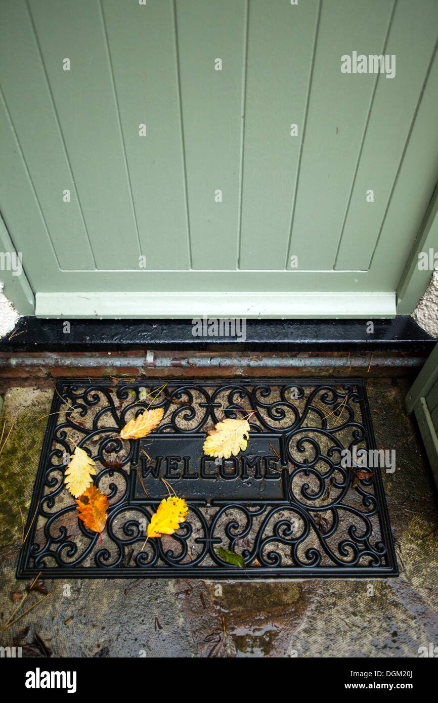 Buntes Herbstlaub, die auf eine willkommene Matte vor einer Hütte Tür mit den Worten willkommen auf die Matte gefallen haben Stockfoto