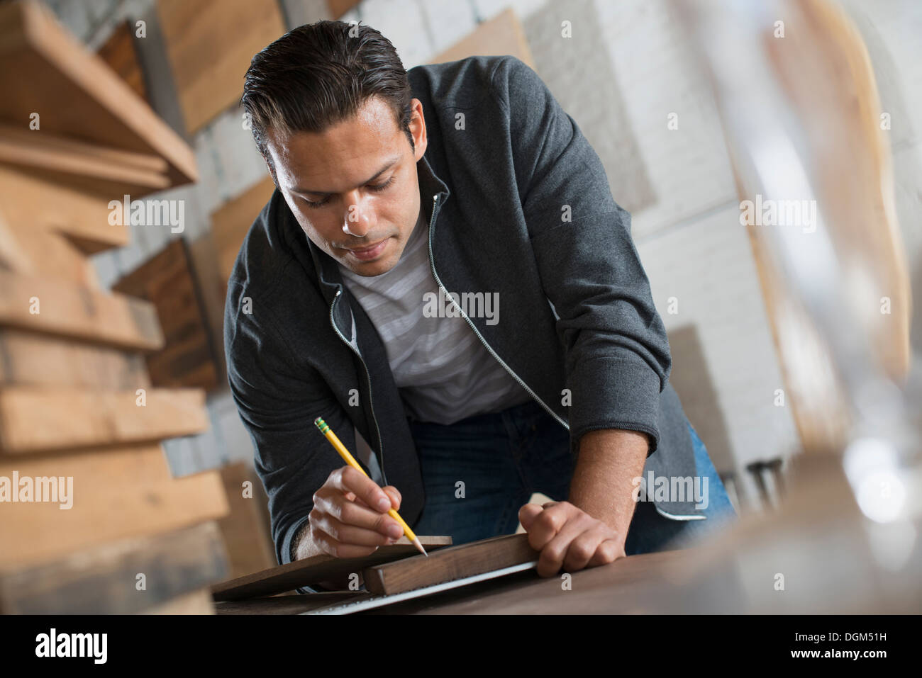 Ein junger Mann in einer Werkstatt, die recycelt und aufgearbeiteten Holz mit Papier und Stift, Aufzeichnungen verwendet. Stockfoto