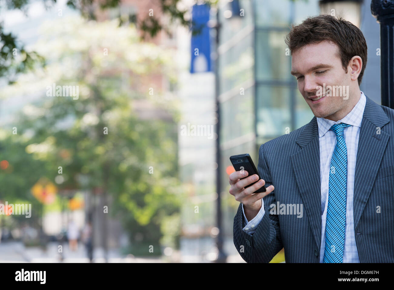 Sommer. Ein junger Mann in einem grauen Anzug und blaue Krawatte. Verwenden ein smart Phone. Stockfoto