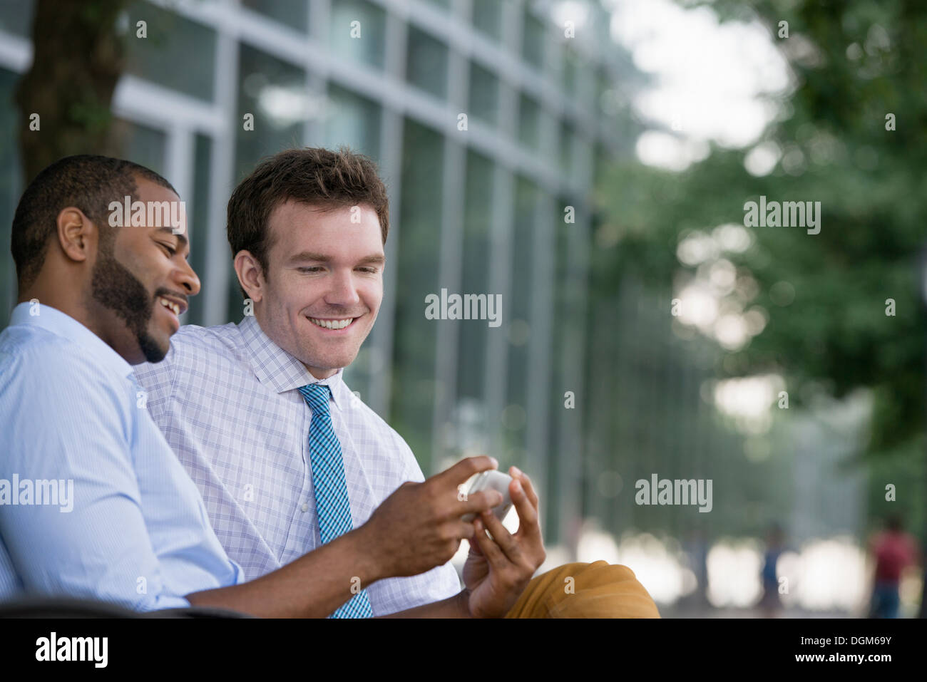Sommer. Zwei Männer sitzen auf einer Bank mit einem Smartphone. Stockfoto