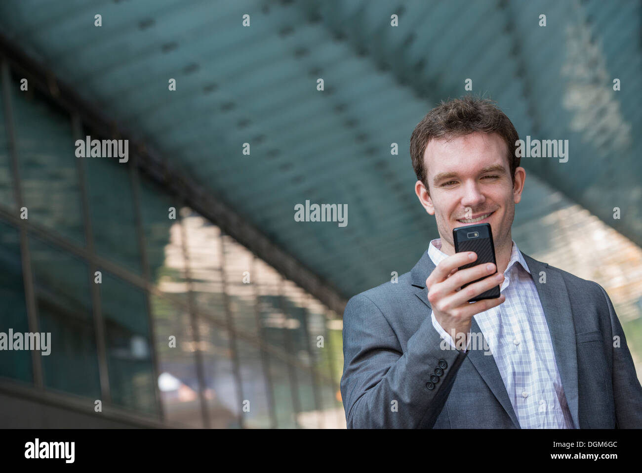 Sommer. Ein junger Mann in einem grauen Anzug und blaue Krawatte. Verwenden ein smart Phone. Stockfoto