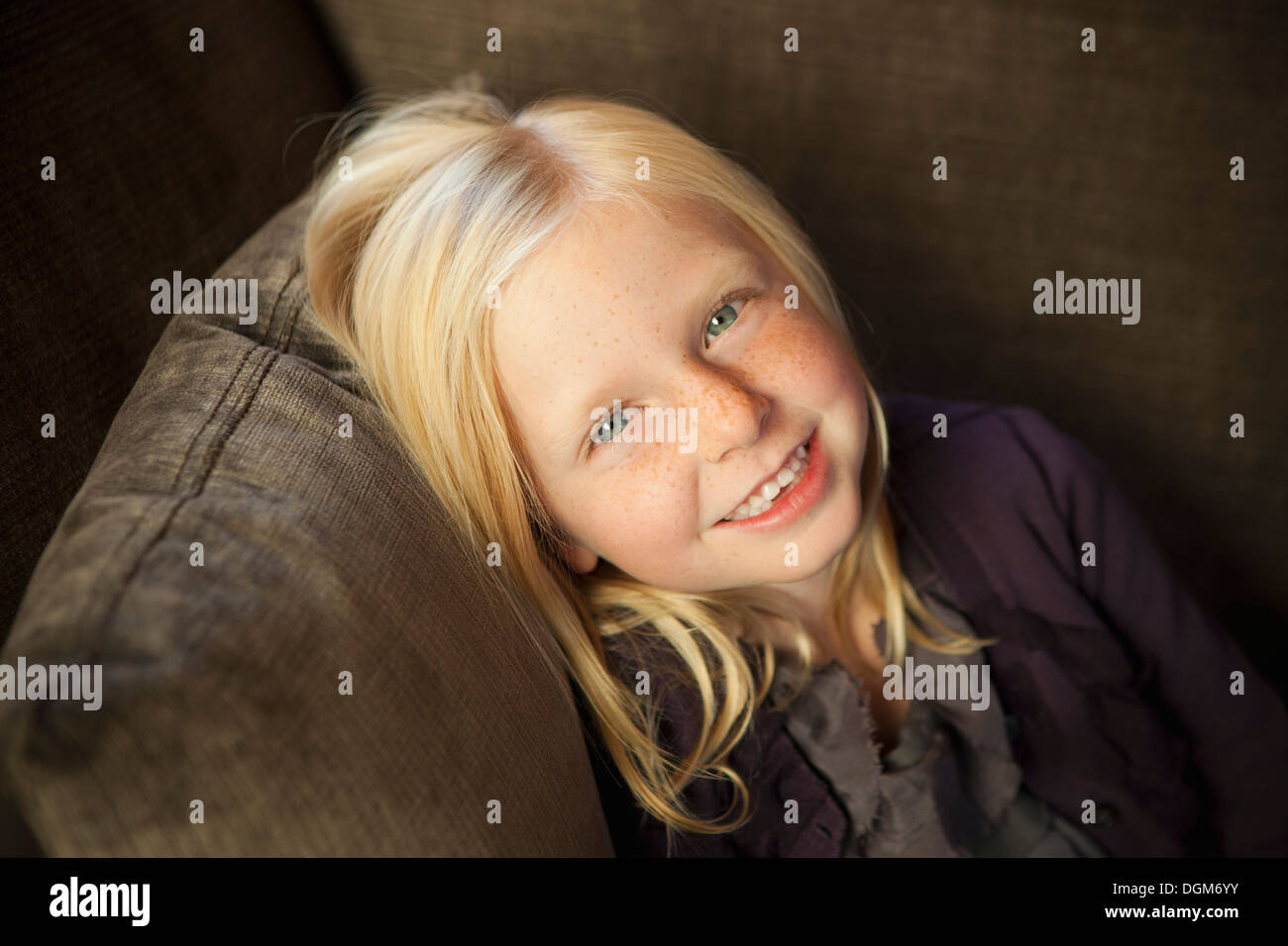 Ein Mädchen sitzt auf einer Couch, lächelnd in die Kamera. Stockfoto