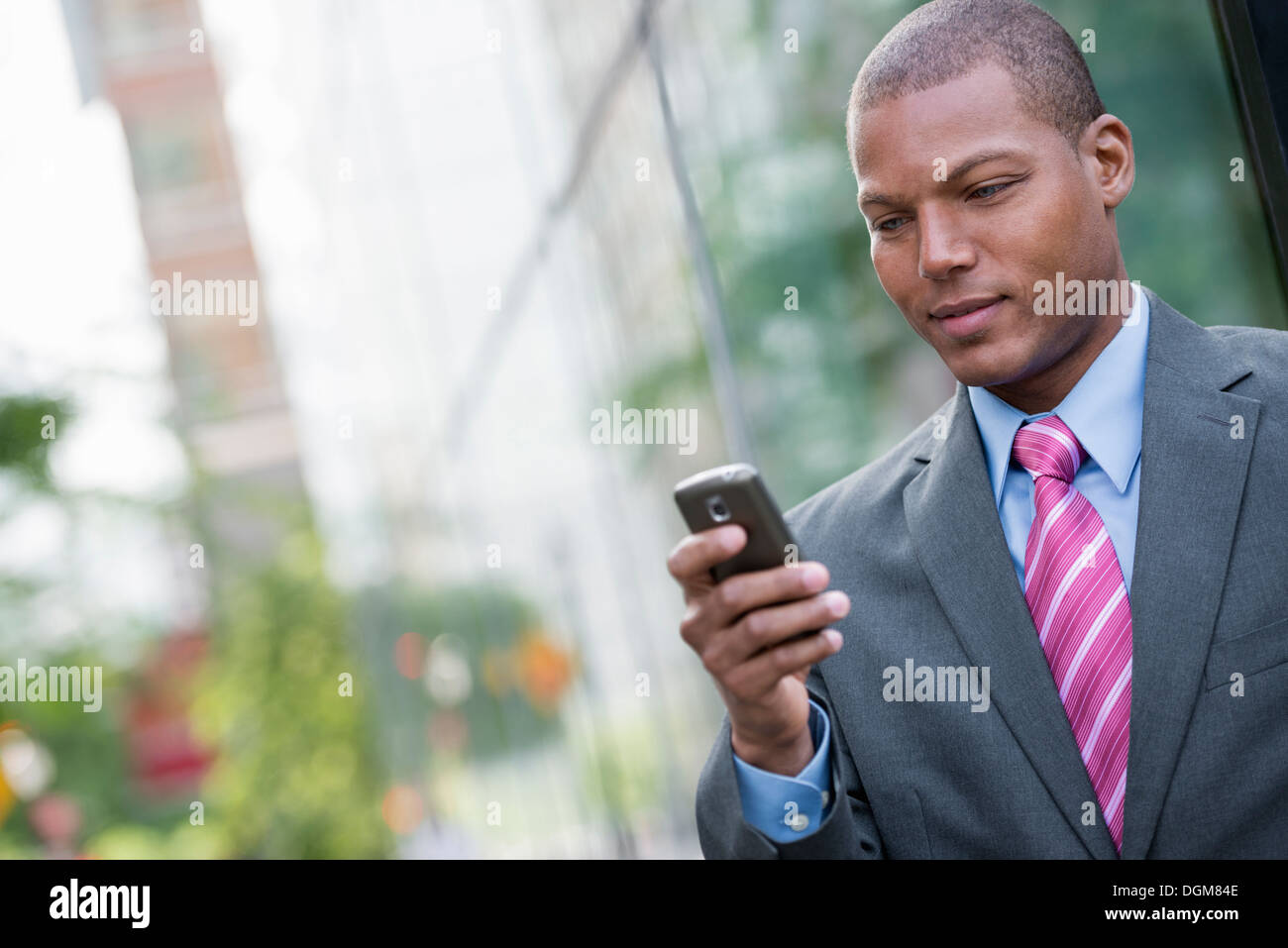 Ein junger Mann in einem Business-Anzug, ein hellblaues Hemd mit roter Krawatte. In einer New-York-City-Straße. Verwenden ein smart Phone. Stockfoto