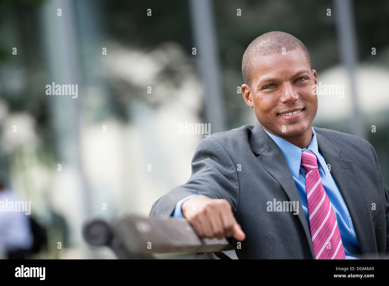 Ein junger Mann in einem Business-Anzug, ein hellblaues Hemd mit roter Krawatte. Auf einer Stadtstraße. Lächelnd in die Kamera. Stockfoto