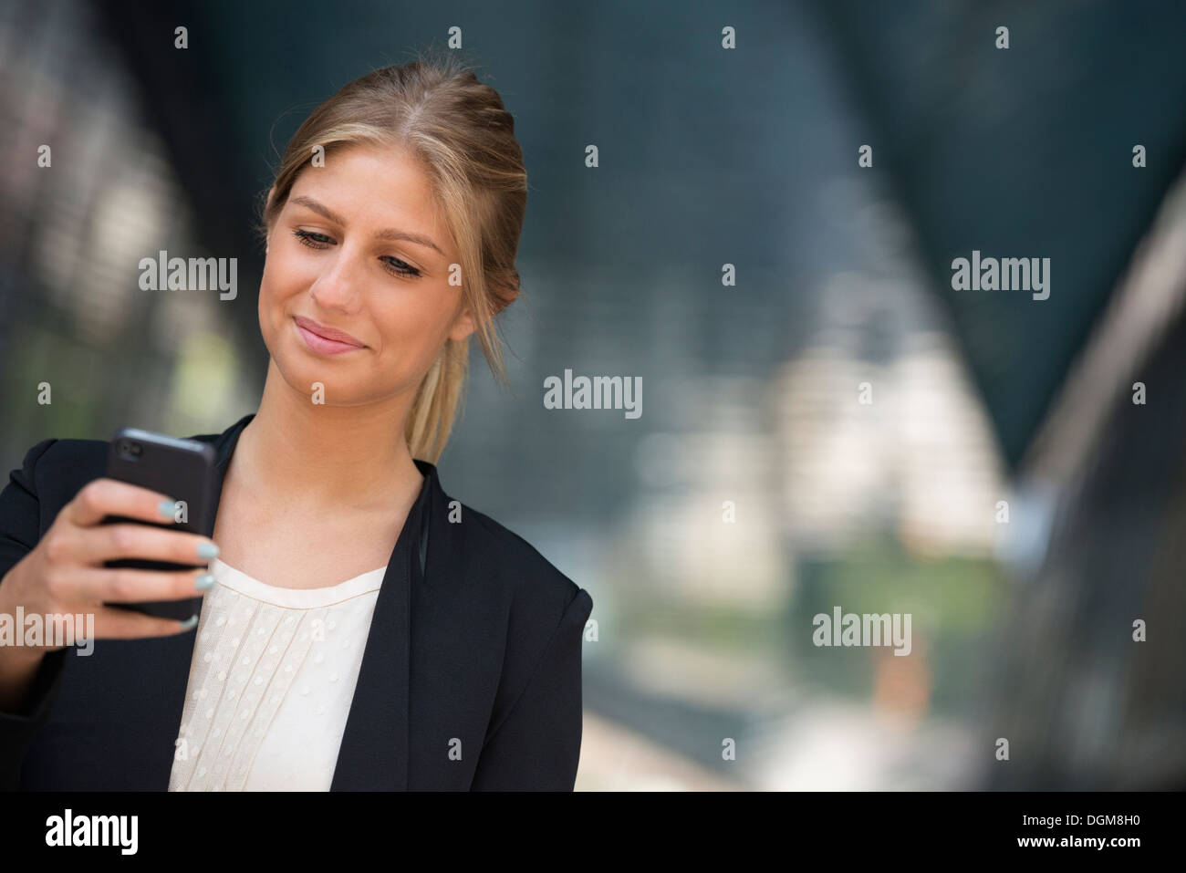 Eine junge blonde Geschäftsfrau in einer New-York-City-Straße. Trug eine schwarze Jacke. Verwenden ein smart Phone. Stockfoto