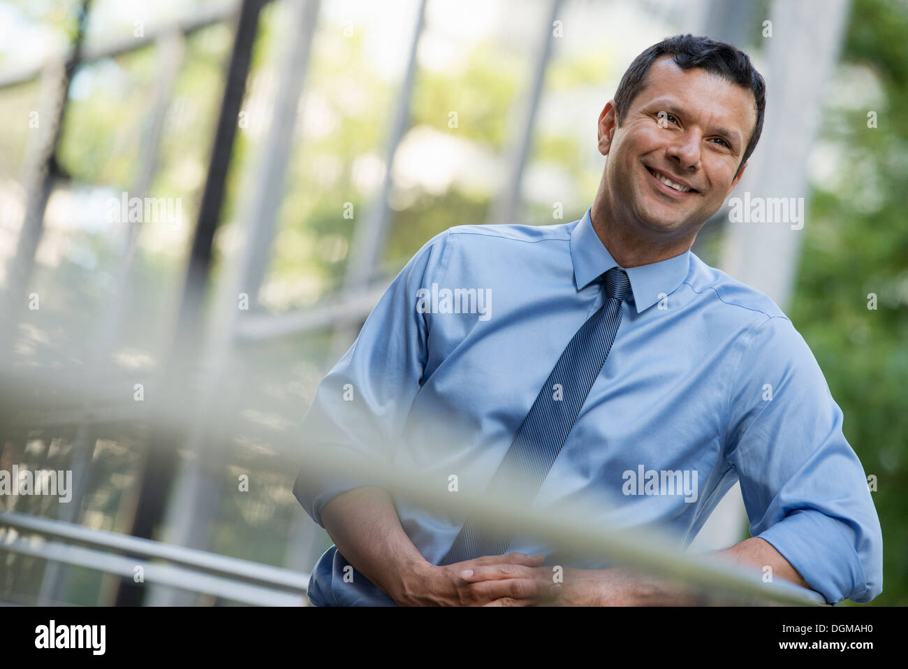 Geschäftsleute im Freien. Ein Latino Geschäftsmann in Hemd und Krawatte, stützte sich auf ein Geländer. Entspannen. Stockfoto