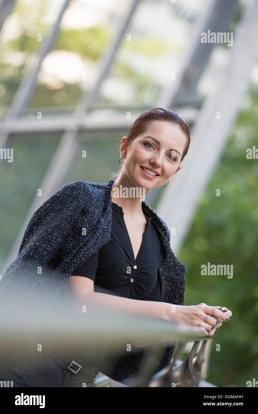 Business-Leute. Eine Frau in eine graue Jacke mit ihrem Haar, stützte sich auf ein Geländer. Stockfoto