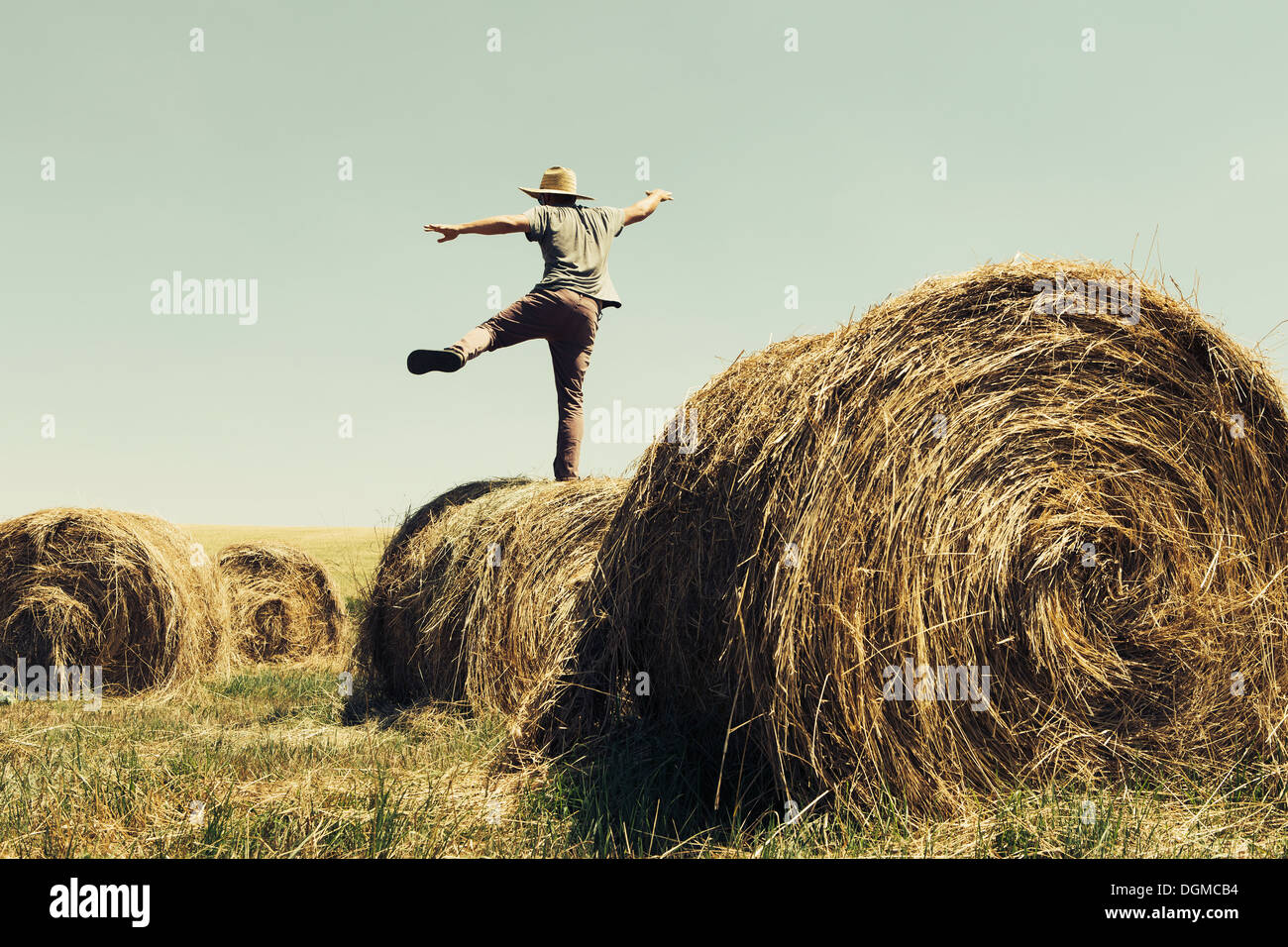 Rückansicht eines Mannes balancieren auf einem Bein auf einem Heuballen. Stockfoto