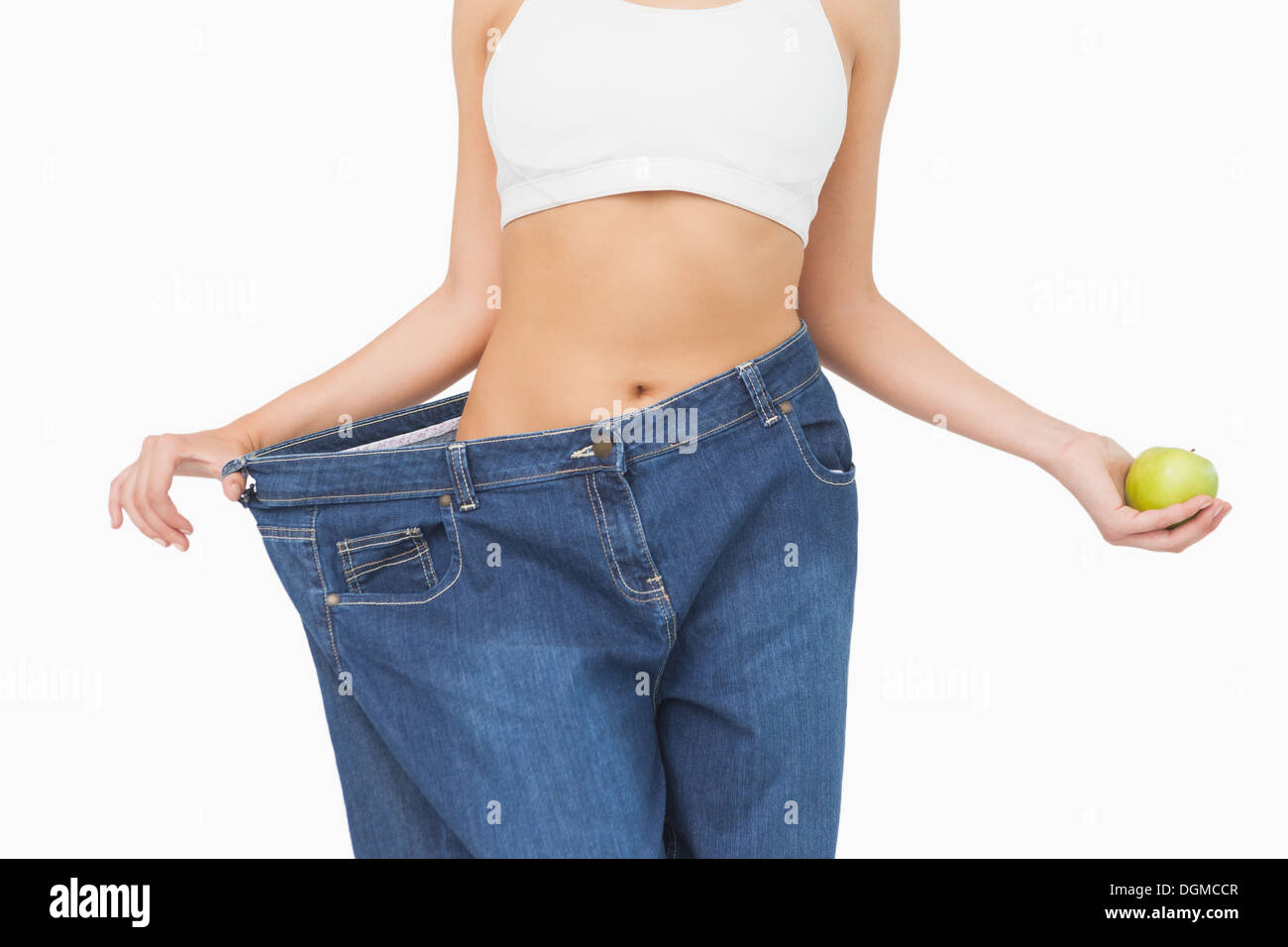 Mittelteil der schlanke Frau trägt zu groß Jeans hält einen Apfel Stockfoto