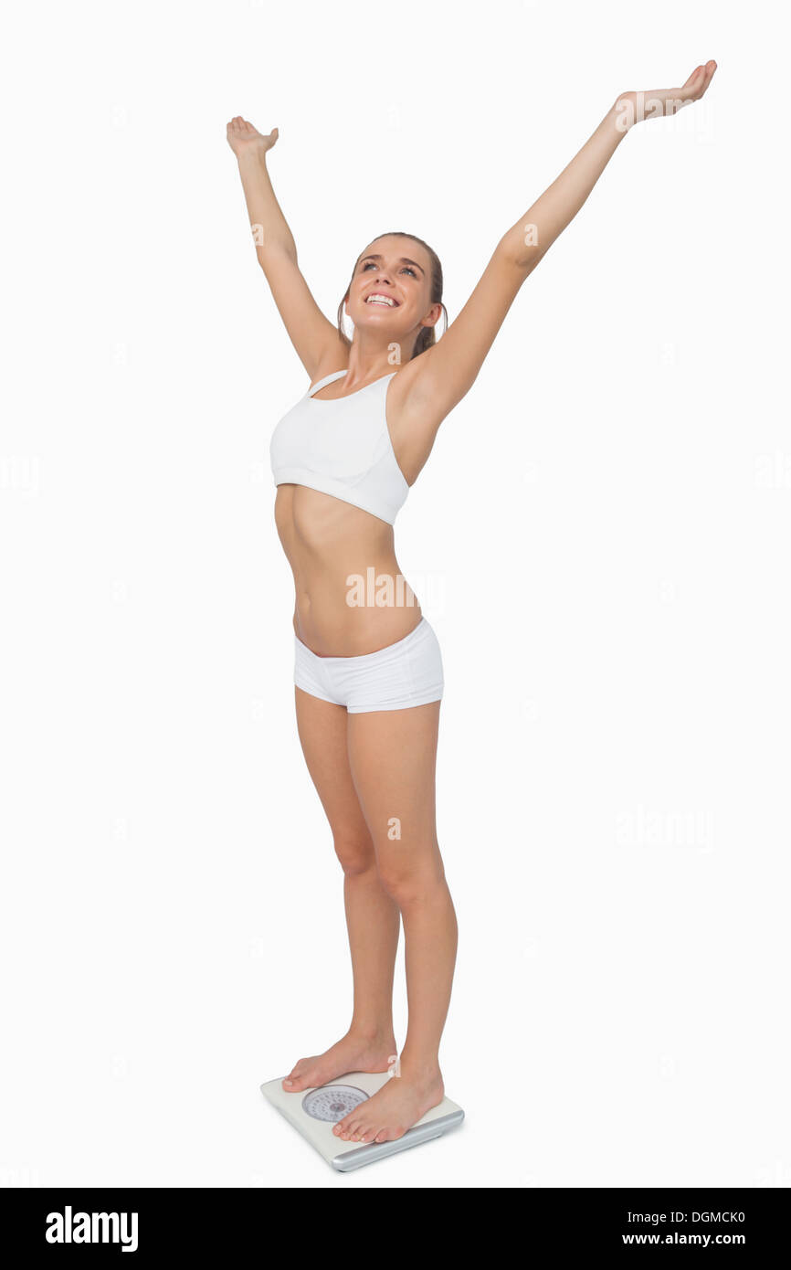 Fröhliche schlanke Frau steht auf eine Waage, die Arme ausbreiten Stockfoto