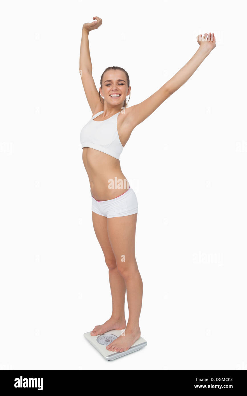 Glücklich schlanke Frau steht auf eine Waage, die ihre Arme ausbreitet Stockfoto