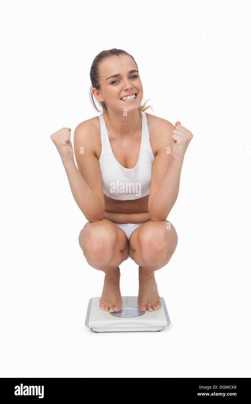 Junge Frau kauert auf einer Waage Stockfoto