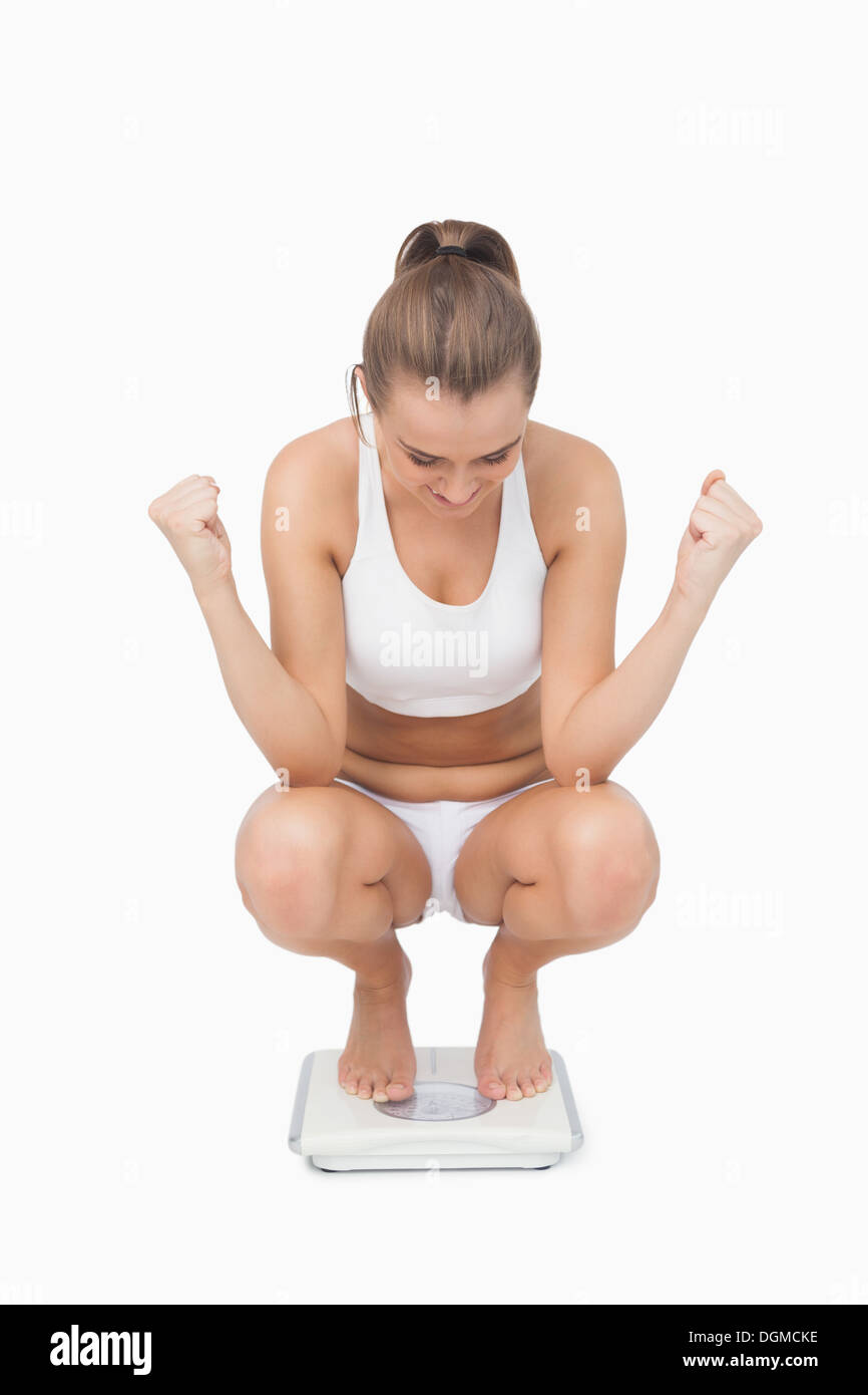 Erfolgreiche junge Frau kauert auf einer Waage Stockfoto