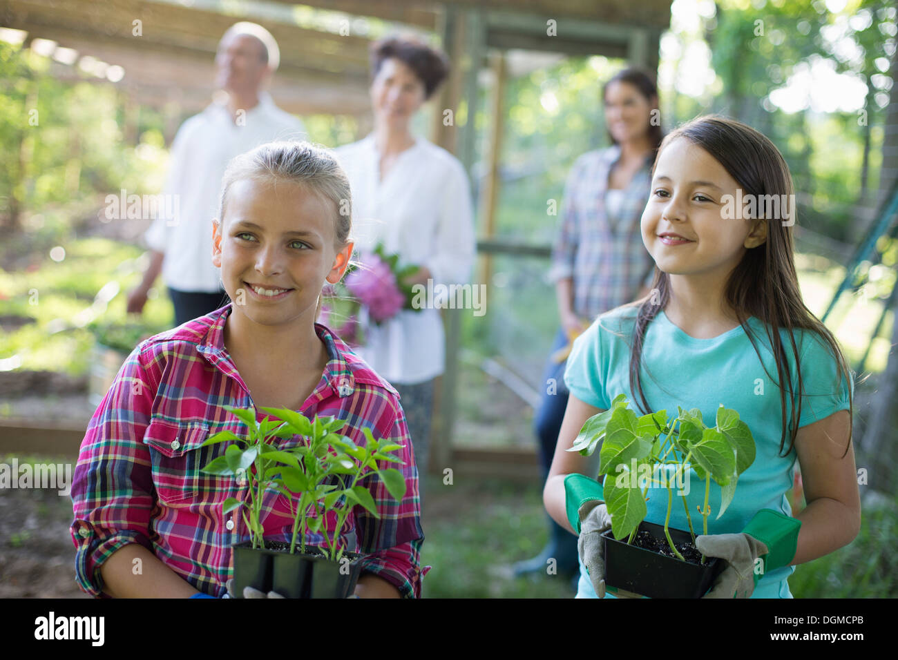 Bio-Bauernhof. Sommer-Party. Zwei Mädchen sitzen halten Jungpflanzen mit ein älteres Paar und eine junge Frau auf der Suche auf. Stockfoto
