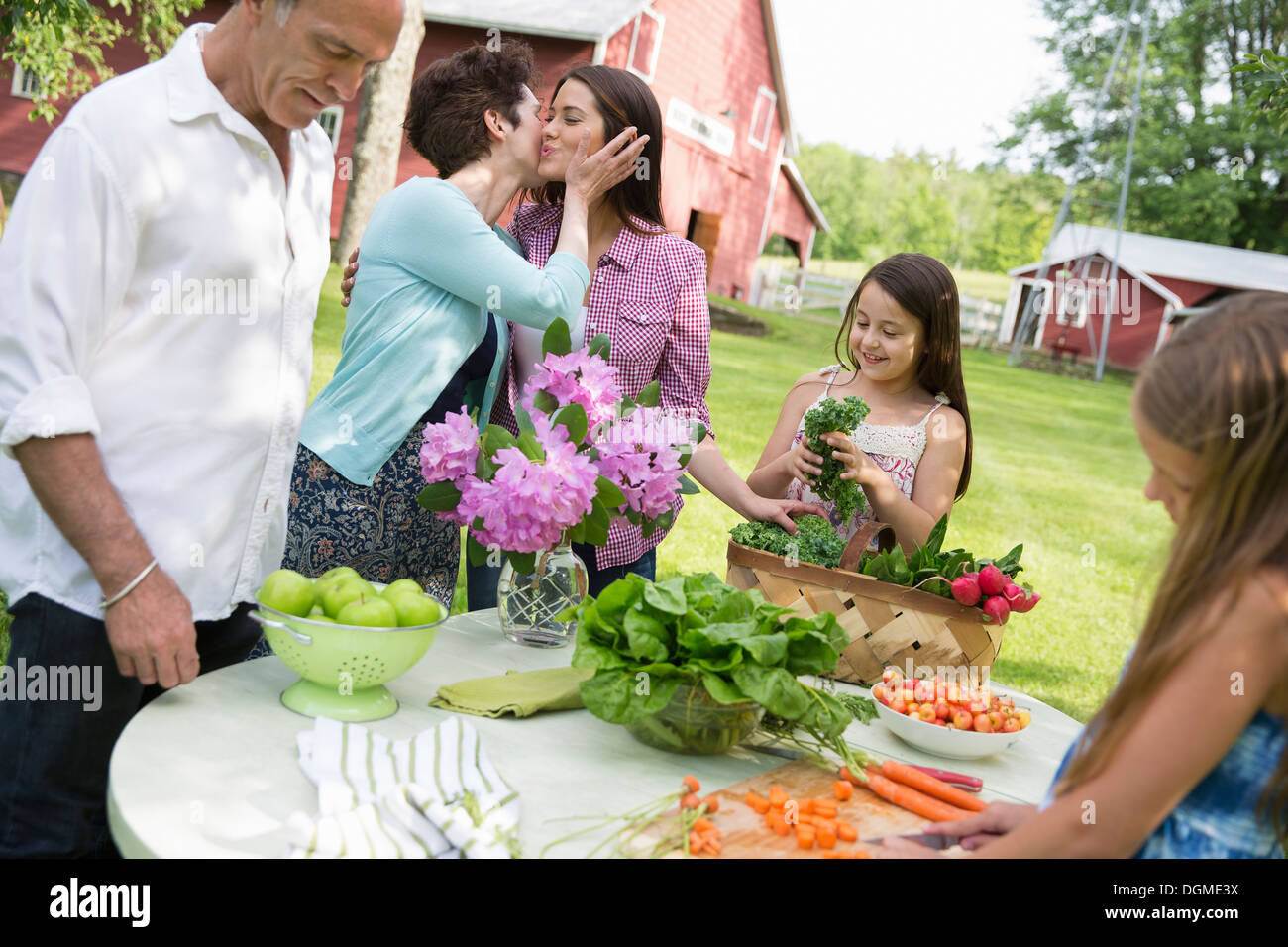 Familienfest. Ein Tisch gedeckt mit Salaten und frischem Obst und Gemüse. Eine Mutter, eine Tochter auf die Wange küssen. Stockfoto