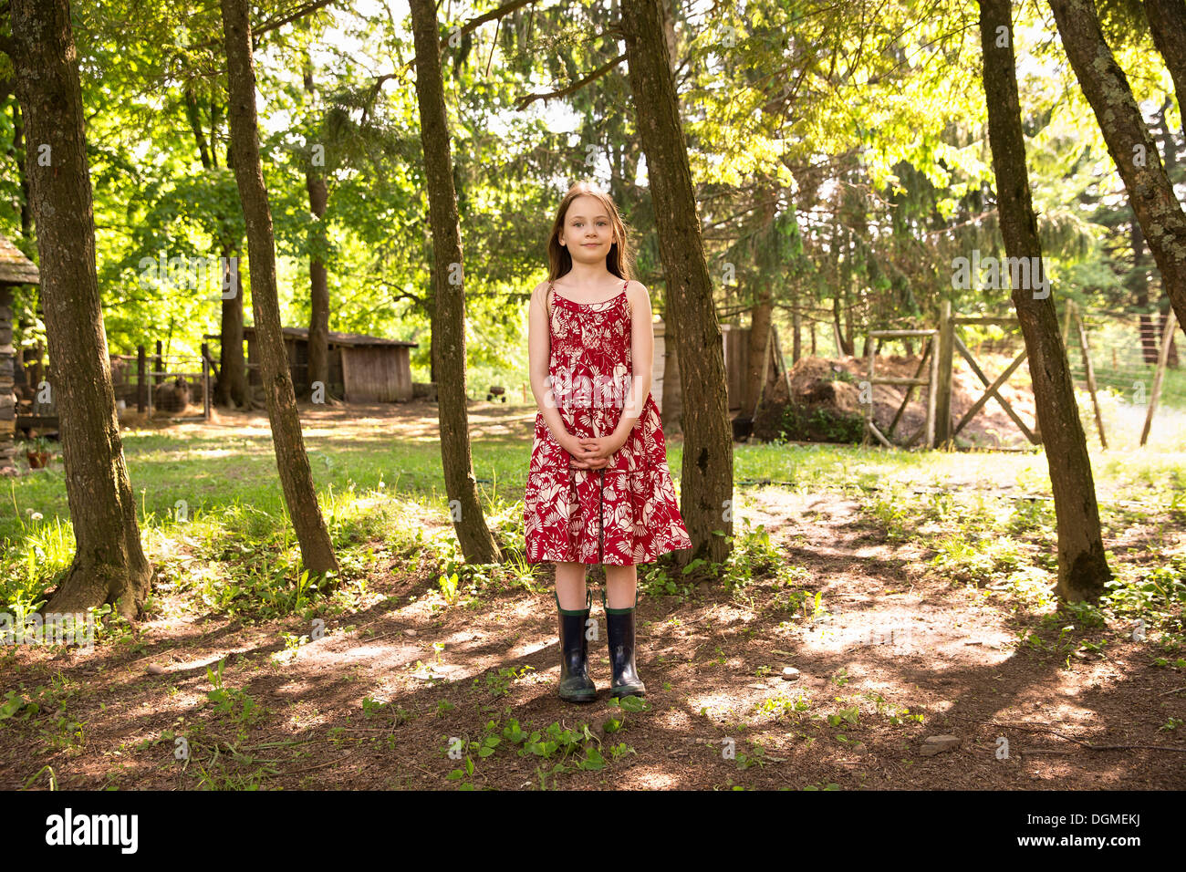 Ein Mädchen in einem Sommerkleid, stehend in einer Baumgruppe. Stockfoto