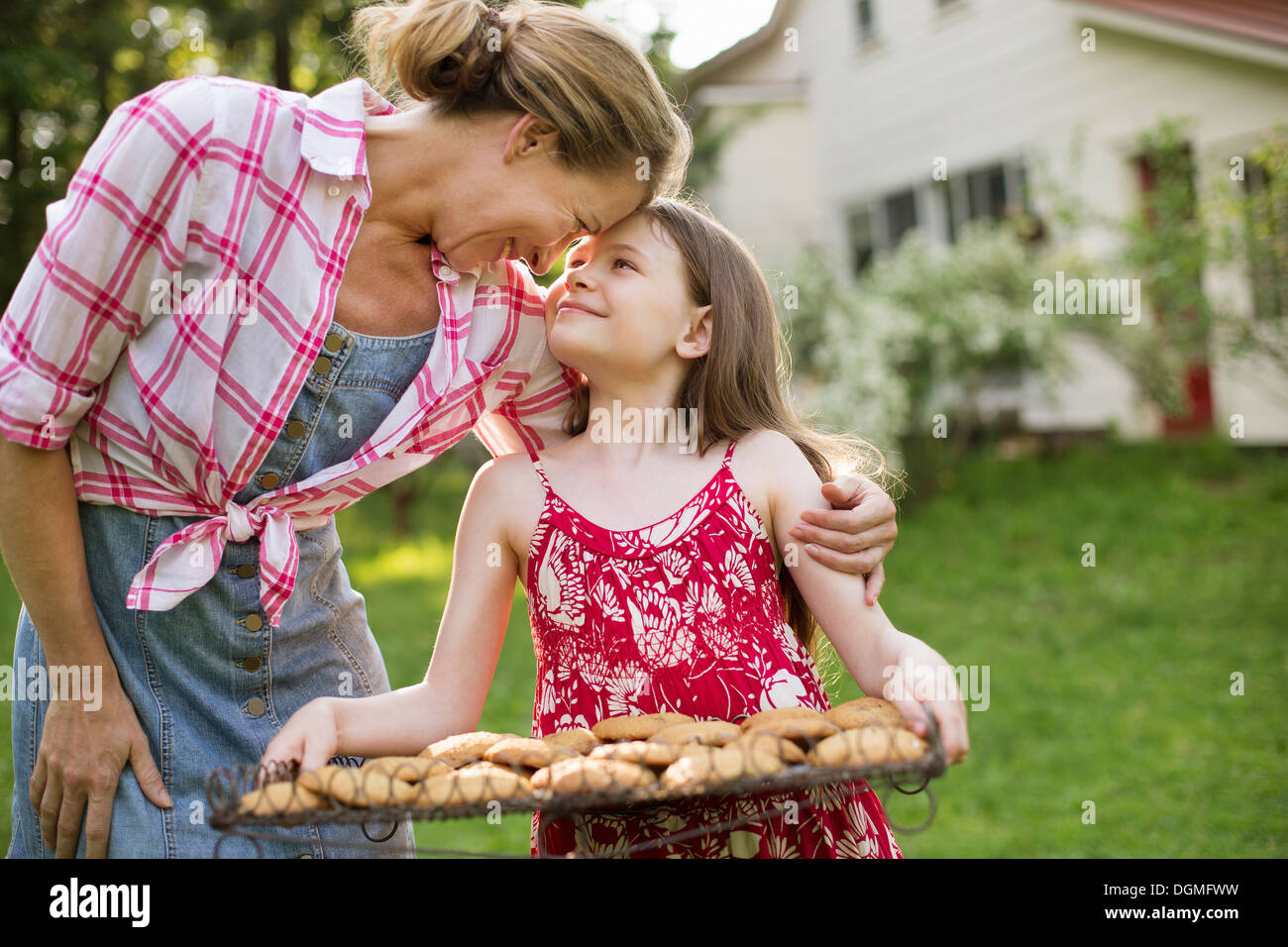 Hausgemachte Kekse backen. Ein junges Mädchen hält ein Tablett mit frisch gebackene Kekse und einer erwachsenen Frau lehnt sich nach unten, um sie zu loben. Stockfoto