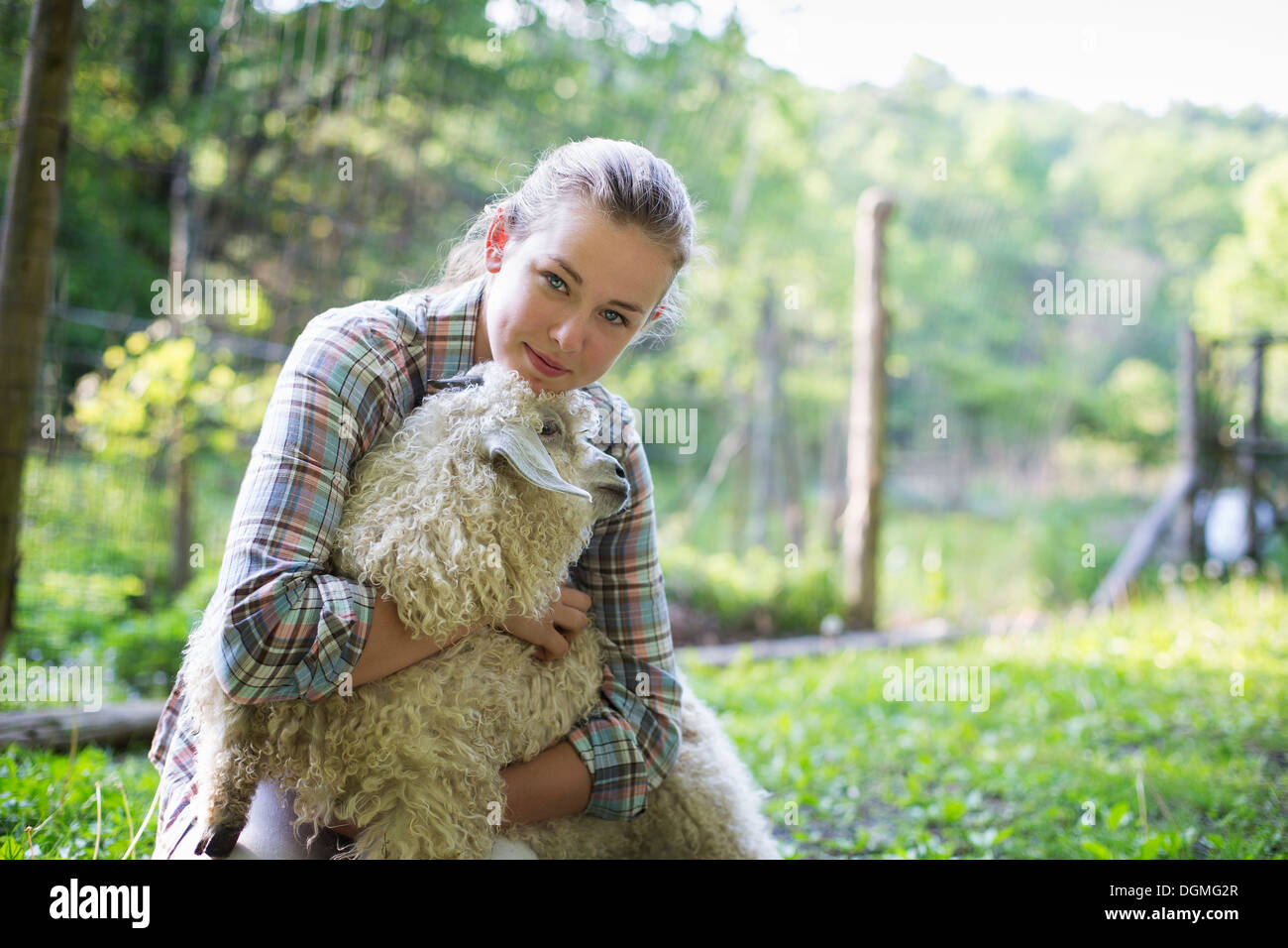 Ein Teenager kniend und legt ihre Arme um eine sehr lockigen Haaren Angora-Ziege. Stockfoto