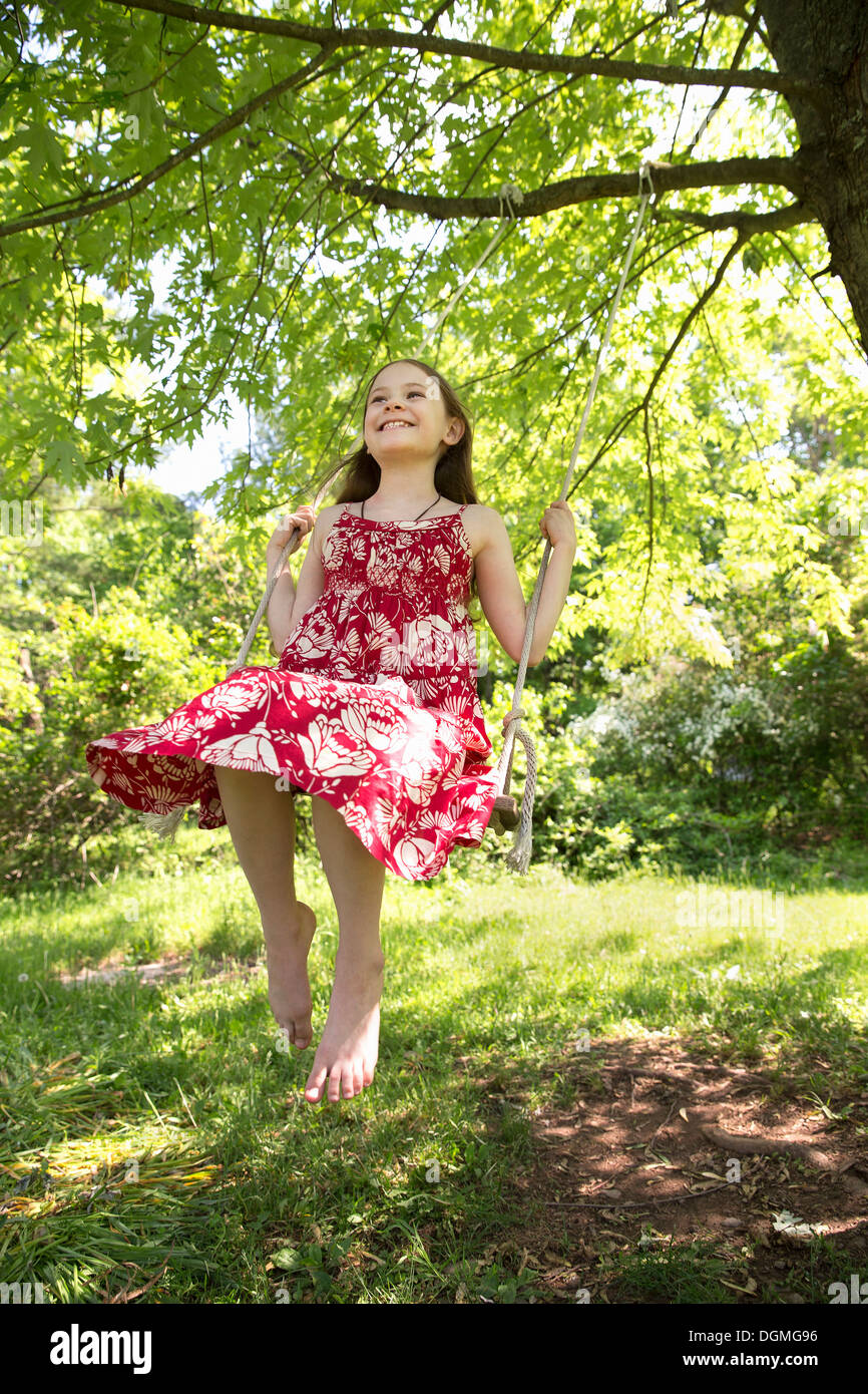 Sommer. Ein Mädchen in einem Sommerkleid auf einer Schaukel schwingen von Ast eines belaubten Baumes. Stockfoto
