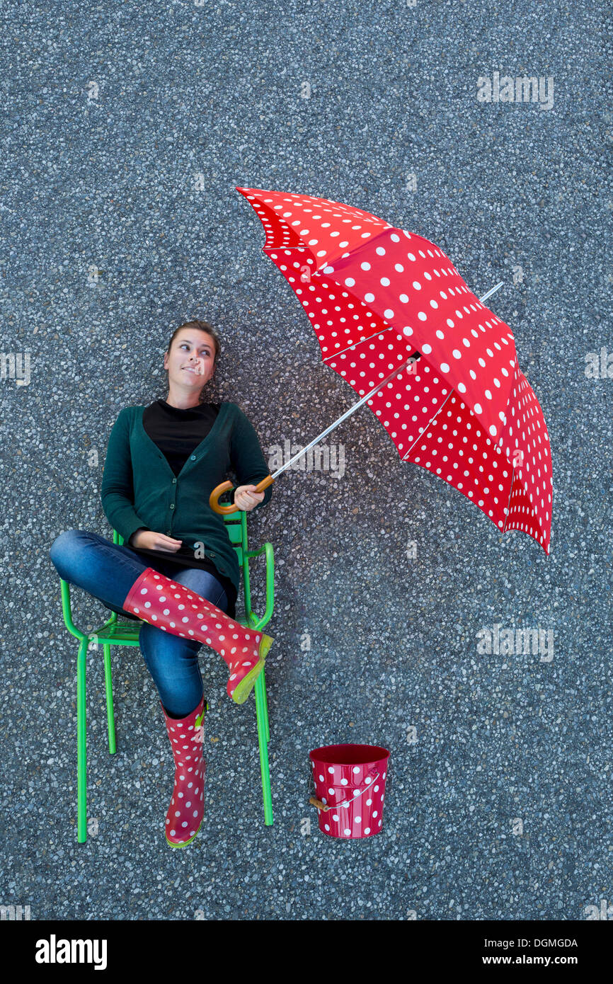 Junge Frau sitzt auf einem Stuhl halten einen gepunkteten Regenschirm, genommen von oben erscheinen Stockfoto
