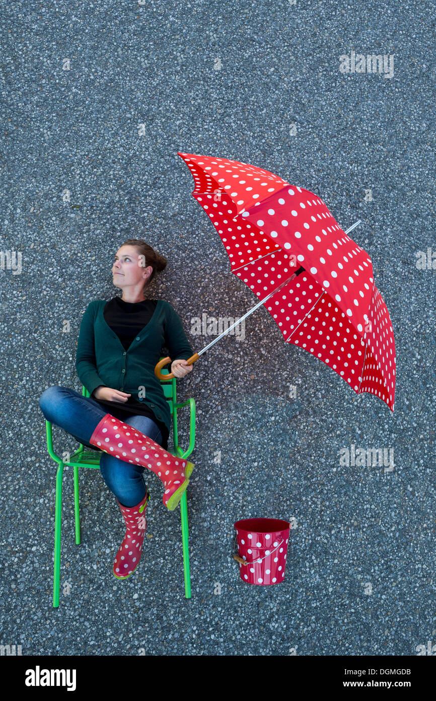 Junge Frau sitzt auf einem Stuhl halten einen gepunkteten Regenschirm, genommen von oben erscheinen Stockfoto