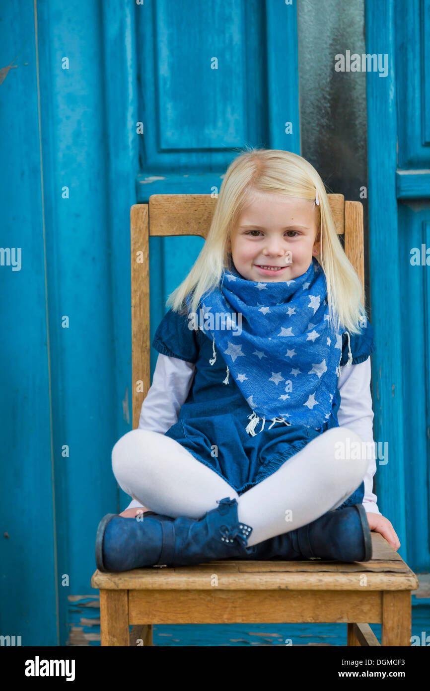 Mädchen, 4 Jahre alt, sitzt vor einer blauen Tür Stockfoto