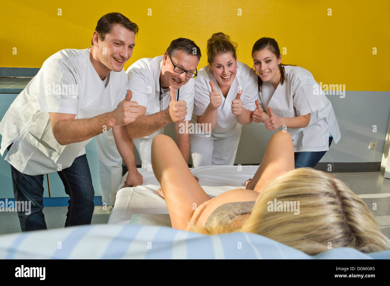 Mehrere Ärzte und Hebammen, die Förderung einer Frau während der Geburt mit ihren Daumen hoch, Deutschland Stockfoto