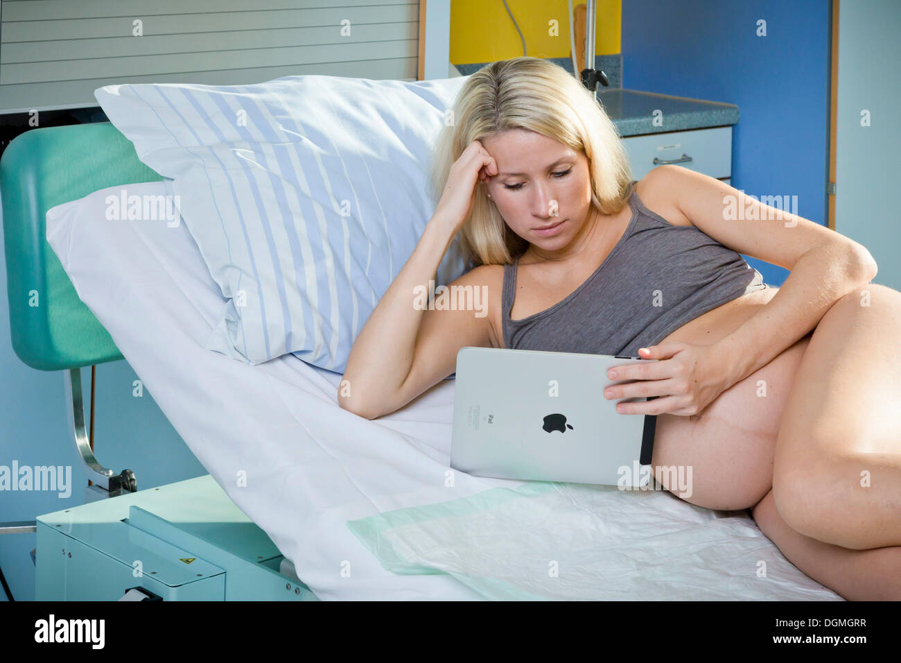Schwangere Frau im Kreißsaal auf die Lieferung Bett liegend und mit Blick auf einen Tablet-PC, Deutschland Stockfoto