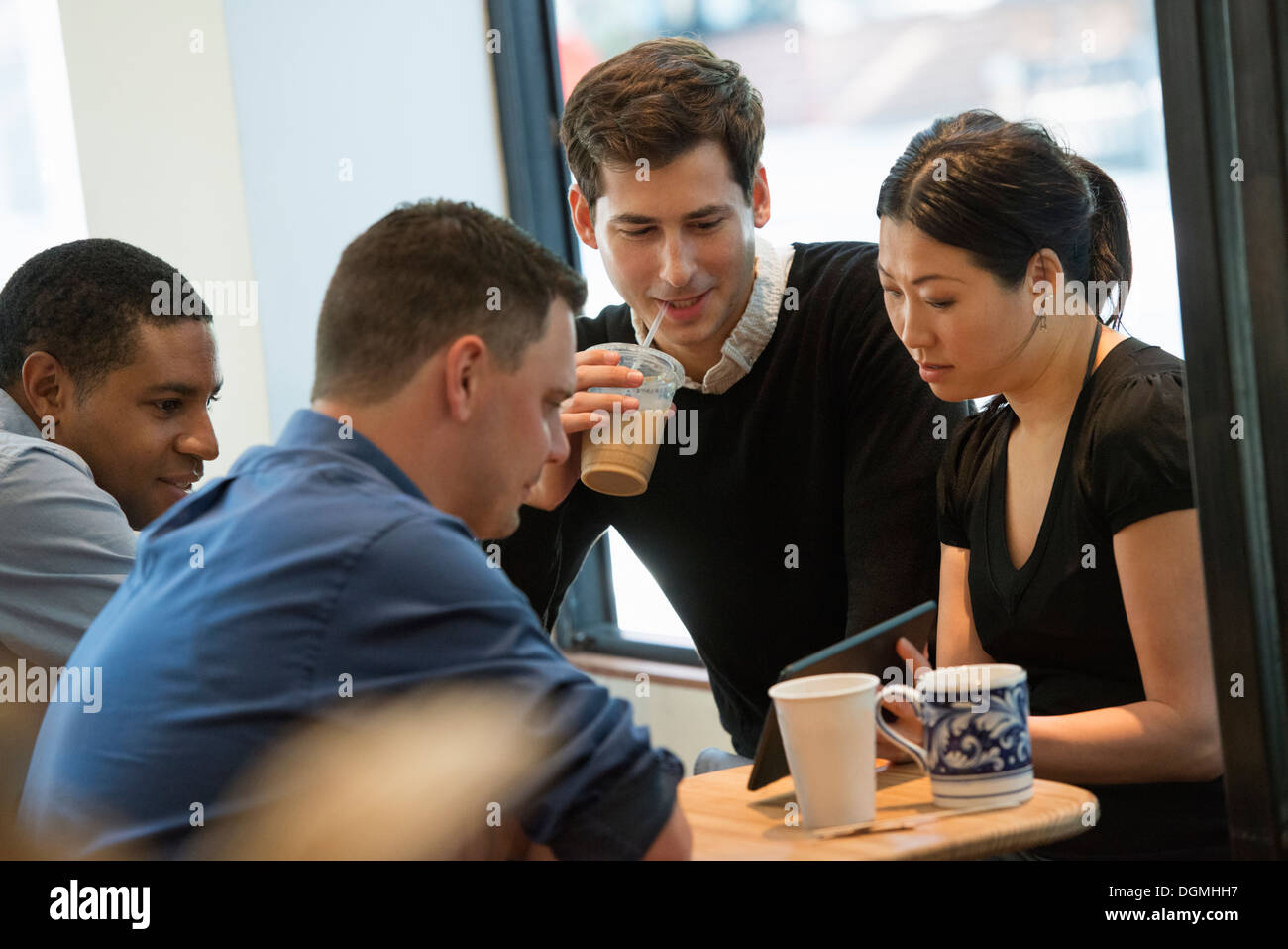 Eine Gruppe von Menschen an einem Tisch in einem Café sitzen. Blick auf den Bildschirm von einem digital-Tablette. Drei Männer und eine Frau. Stockfoto
